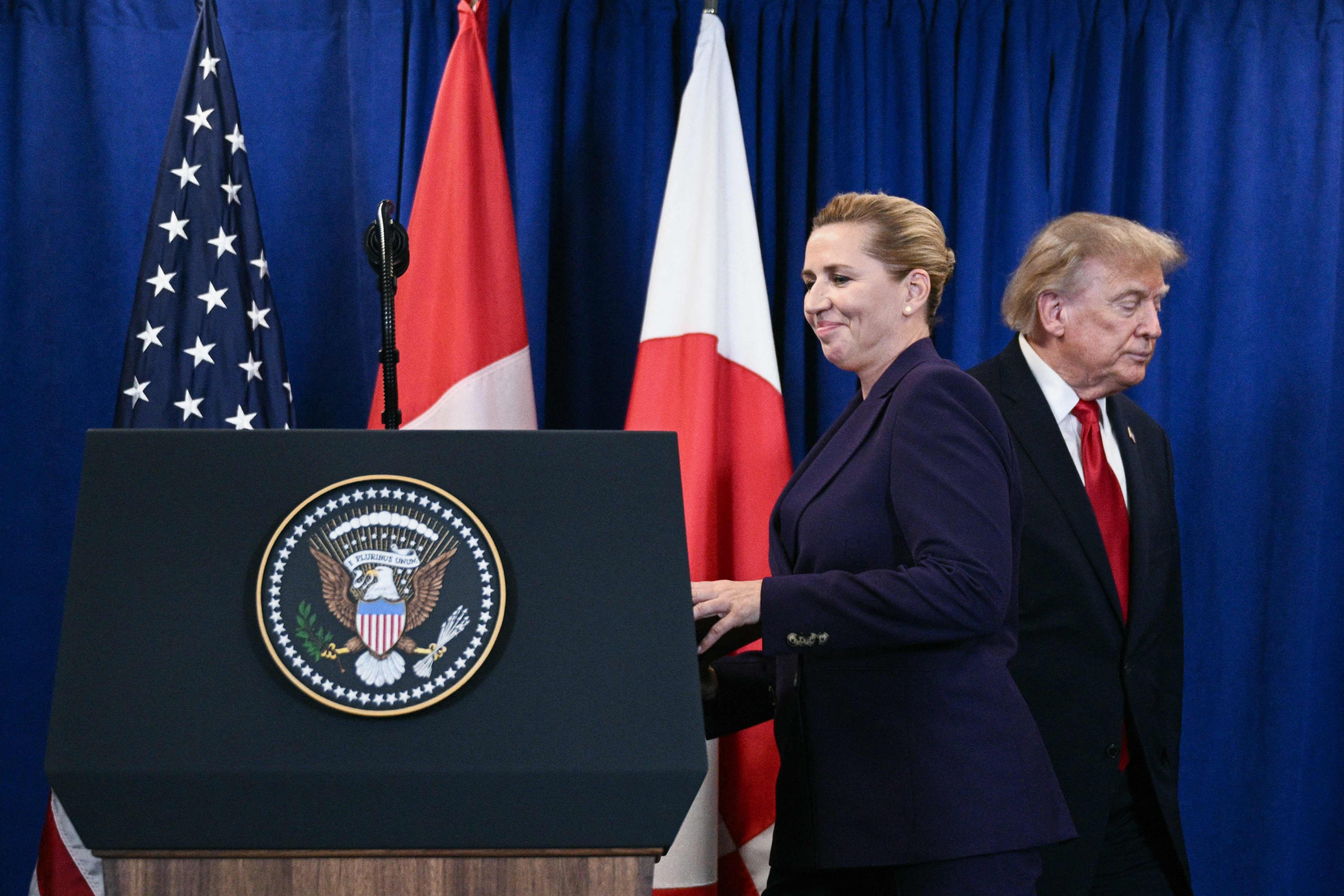 Zwei Personen stehen vor Flaggen und einem Rednerpult mit dem US-Präsidialsiegel.