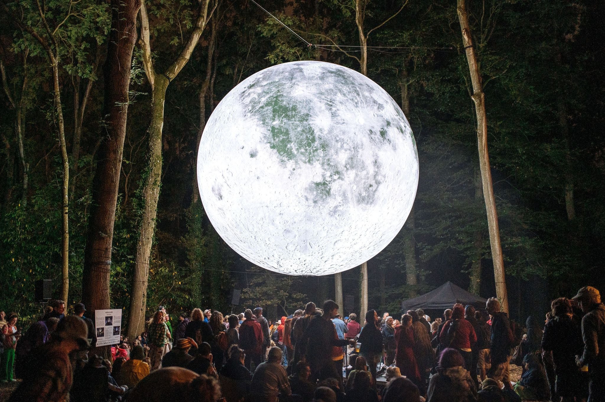 Menschenmenge bestaunt nachts eine große, beleuchtete Mondinstallation im Wald.