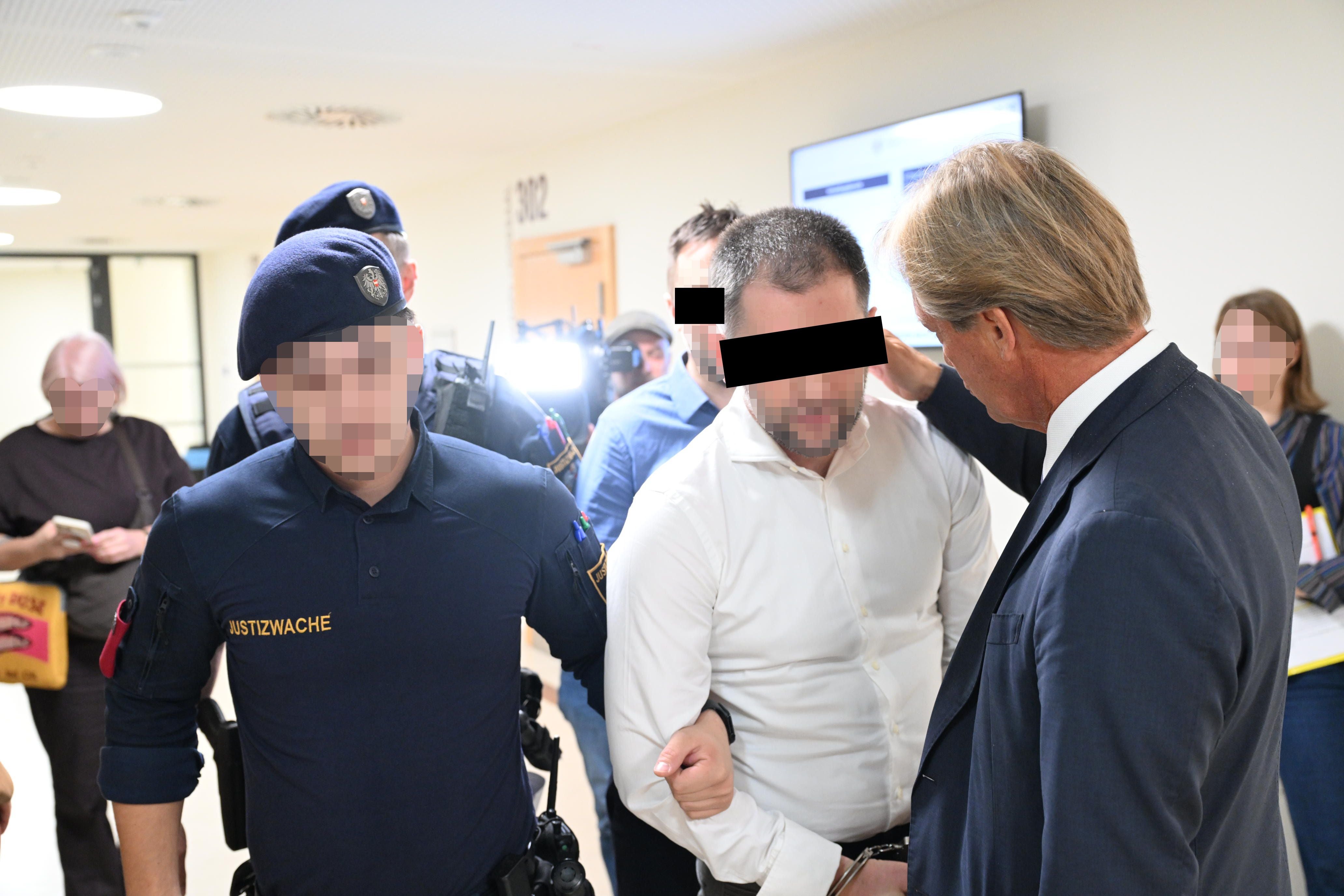 Ein Mann in Handschellen wird von Justizwachebeamten durch einen Gerichtsflur geführt.