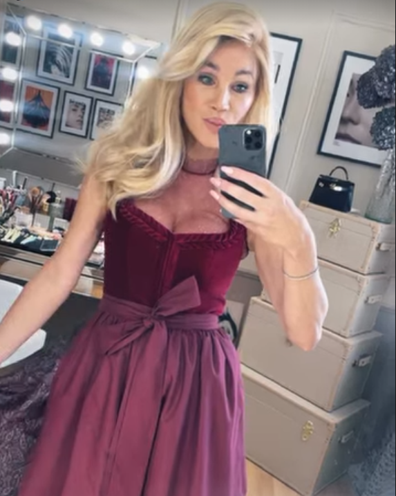 Frau mit blondem Haar trägt ein bordeauxrotes Kleid und macht ein Selfie im Ankleidezimmer.