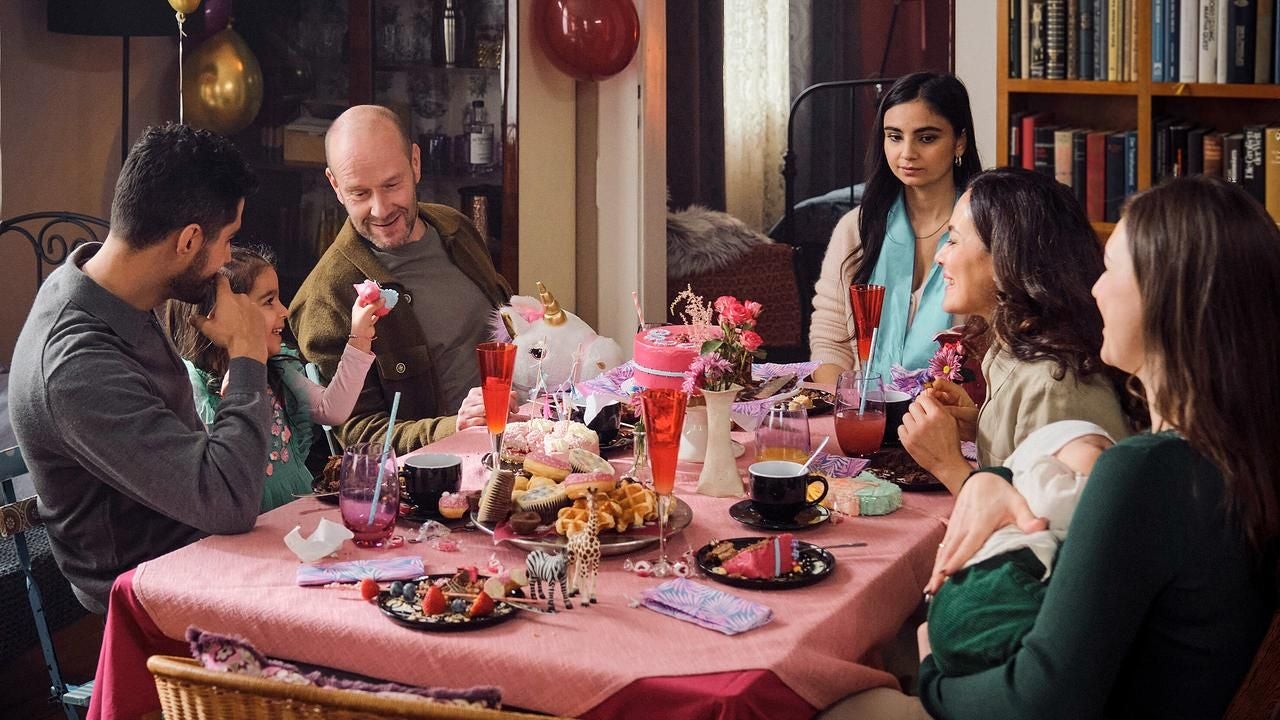 Sechs Personen feiern an einem festlich gedeckten Tisch mit Kuchen und Getränken eine Party.