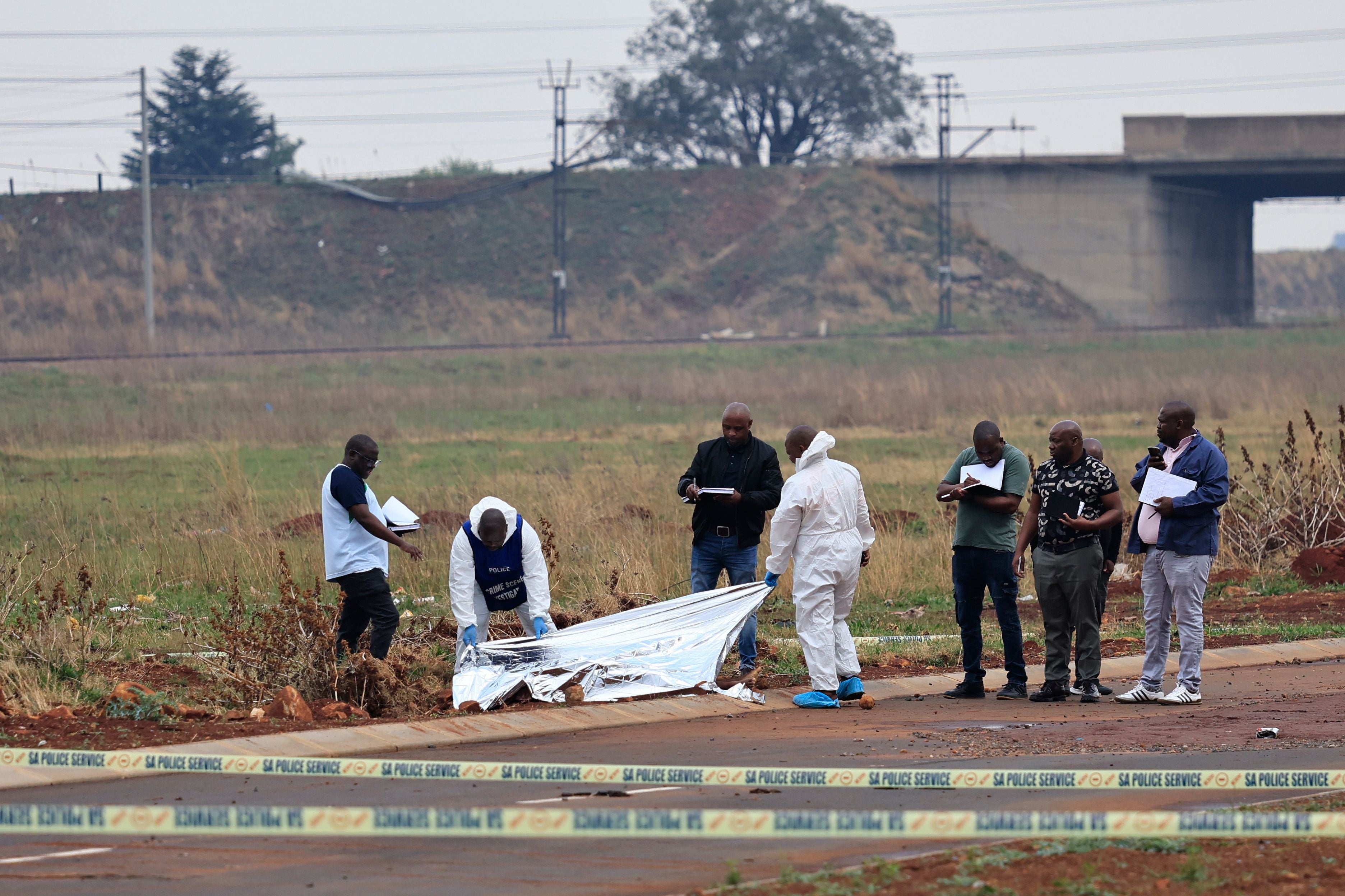 Polizei und Pathologen untersuchen eine Leiche am Straßenrand in Boksburg, Südafrika.