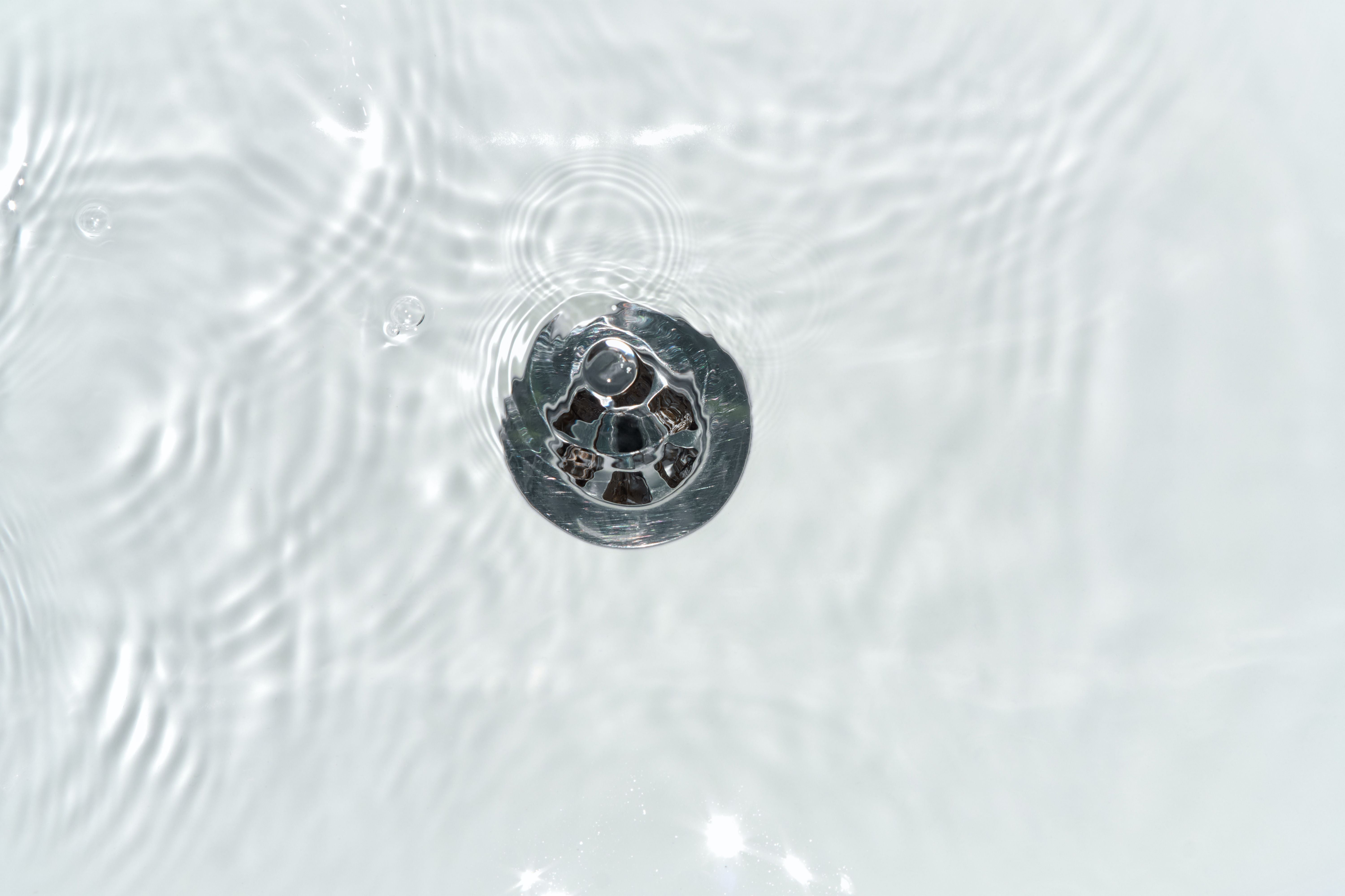 Nahaufnahme eines Abflusses im Wasser mit sanften Wellen und viel freiem, hellem Hintergrund.