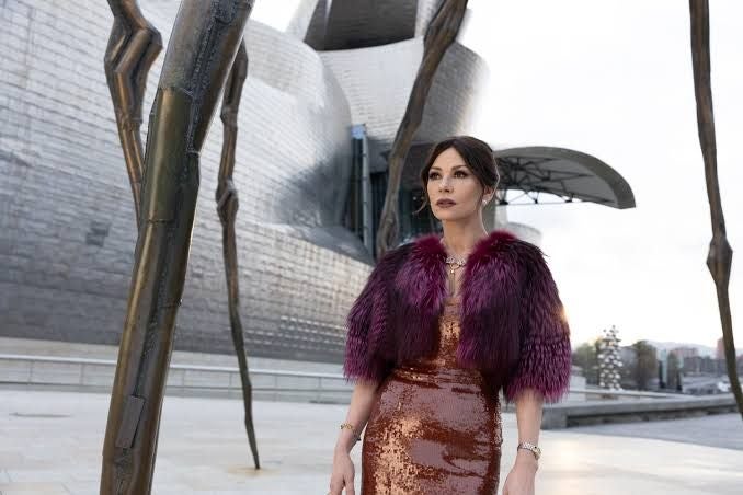 Frau in schimmerndem Kleid steht vor moderner Architektur und Skulpturen im Freien.