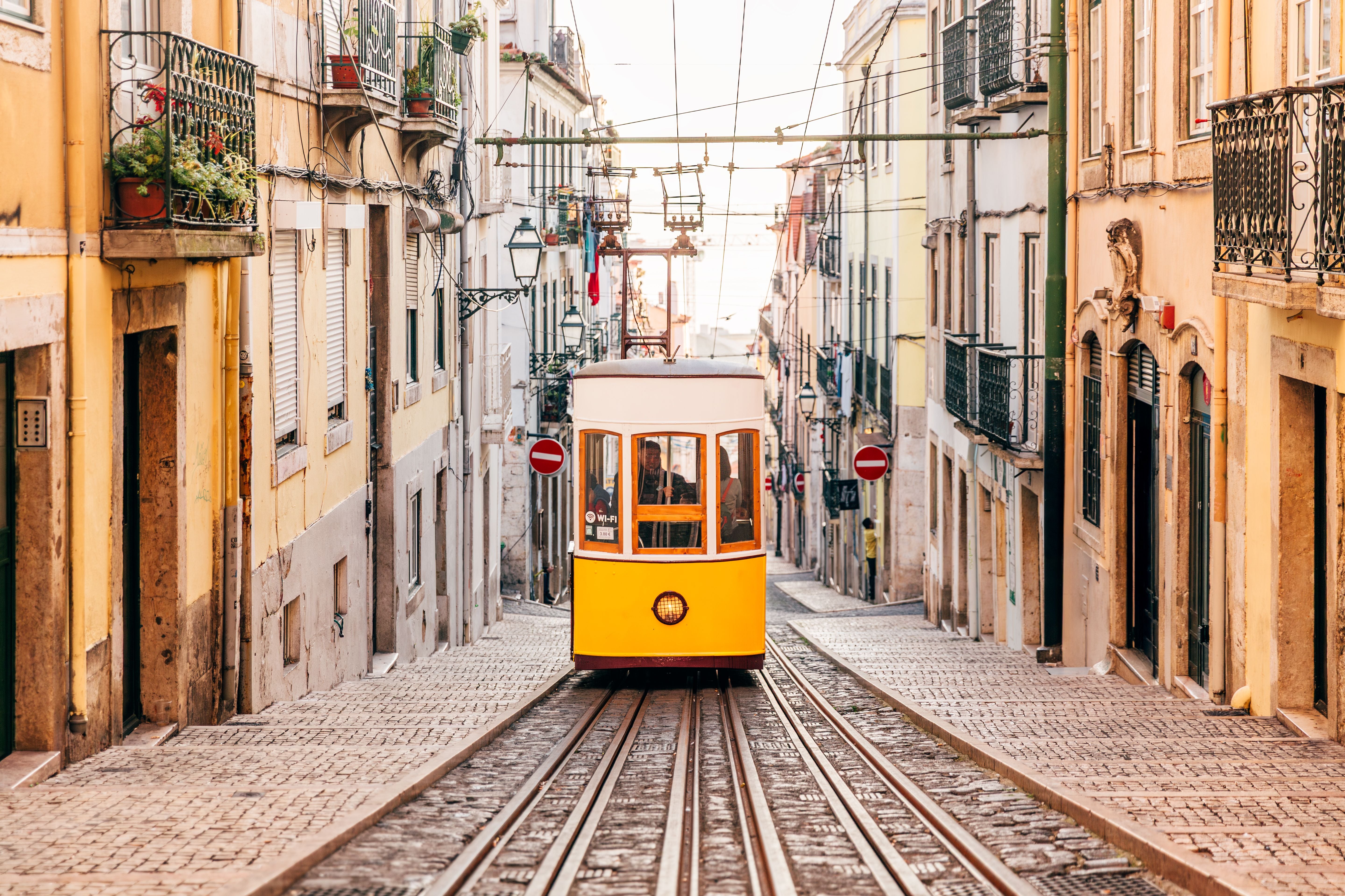 Gelbe Straßenbahn fährt eine enge, steile Gasse mit alten, bunten Häusern in einer Stadt hinunter.