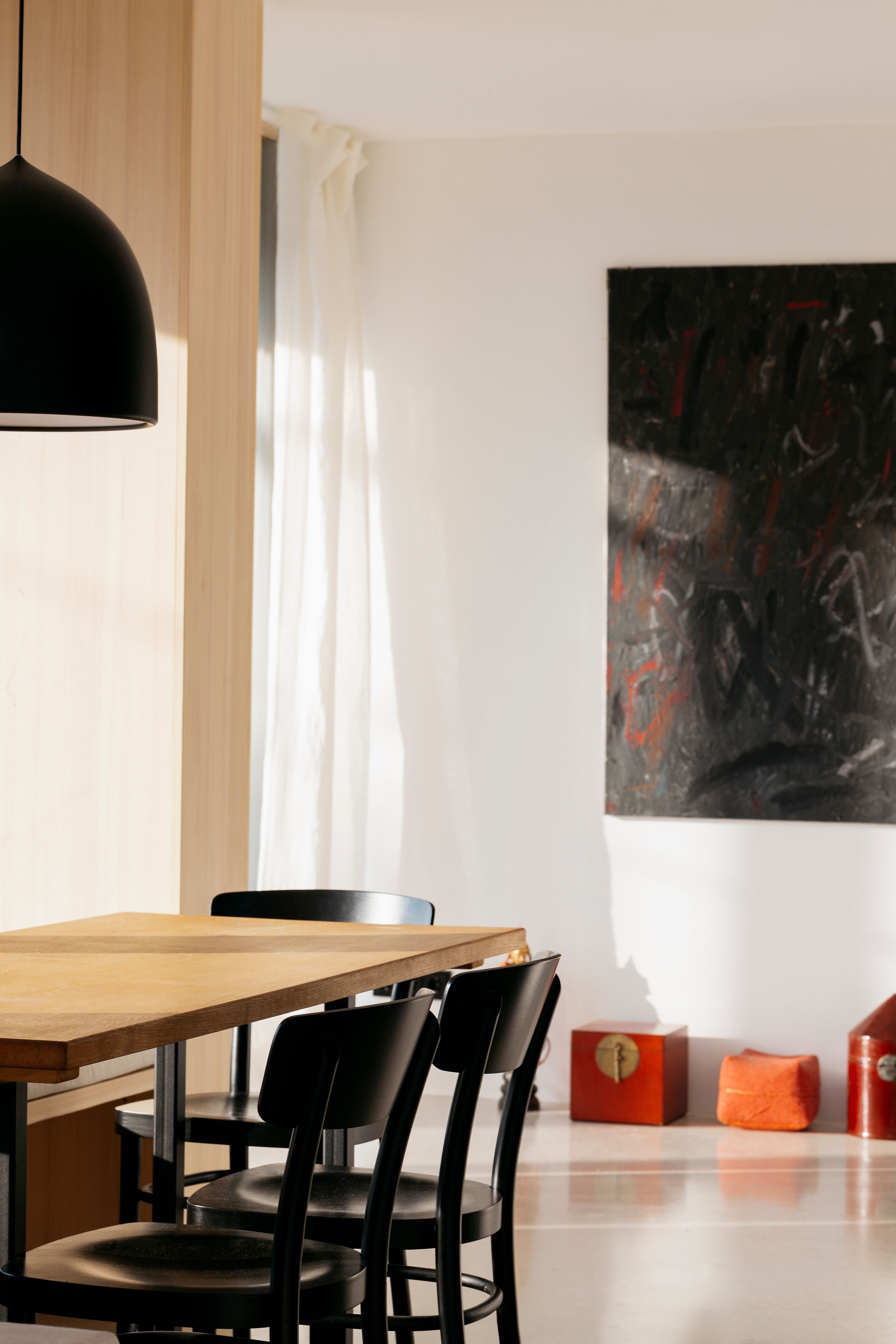 Heller Essbereich mit Holztisch, schwarzen Stühlen und abstraktem Gemälde an der Wand.