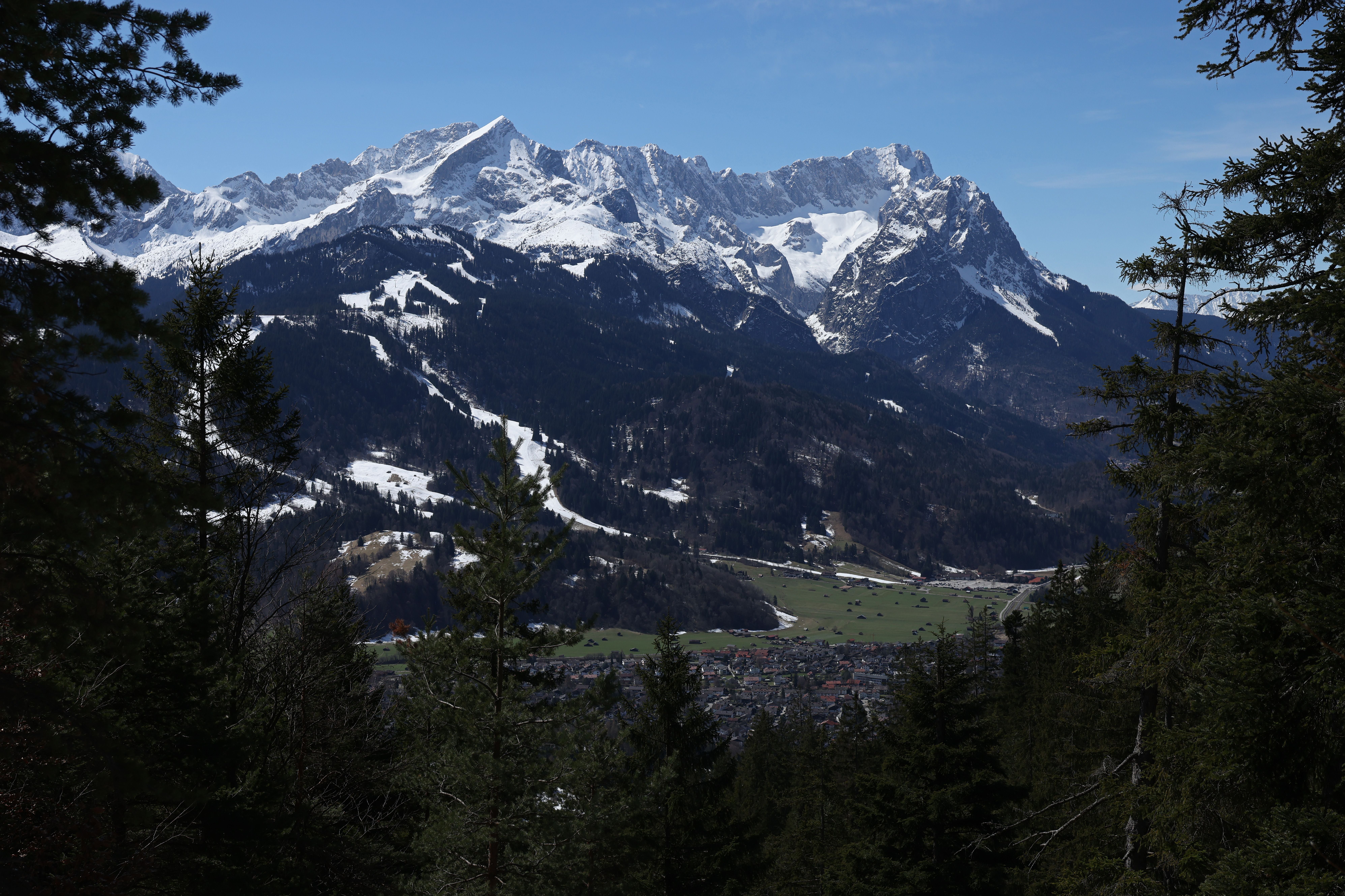 Verschneite Alpengipfel und das Tal von Garmisch-Partenkirchen, eingerahmt von Nadelbäumen.