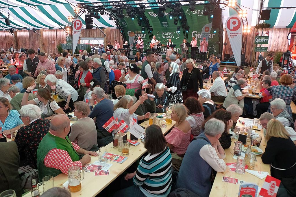 Menschen feiern beim Kaiser Wiesn Fest 2025 in einem Festzelt mit Musikbühne in Wien.