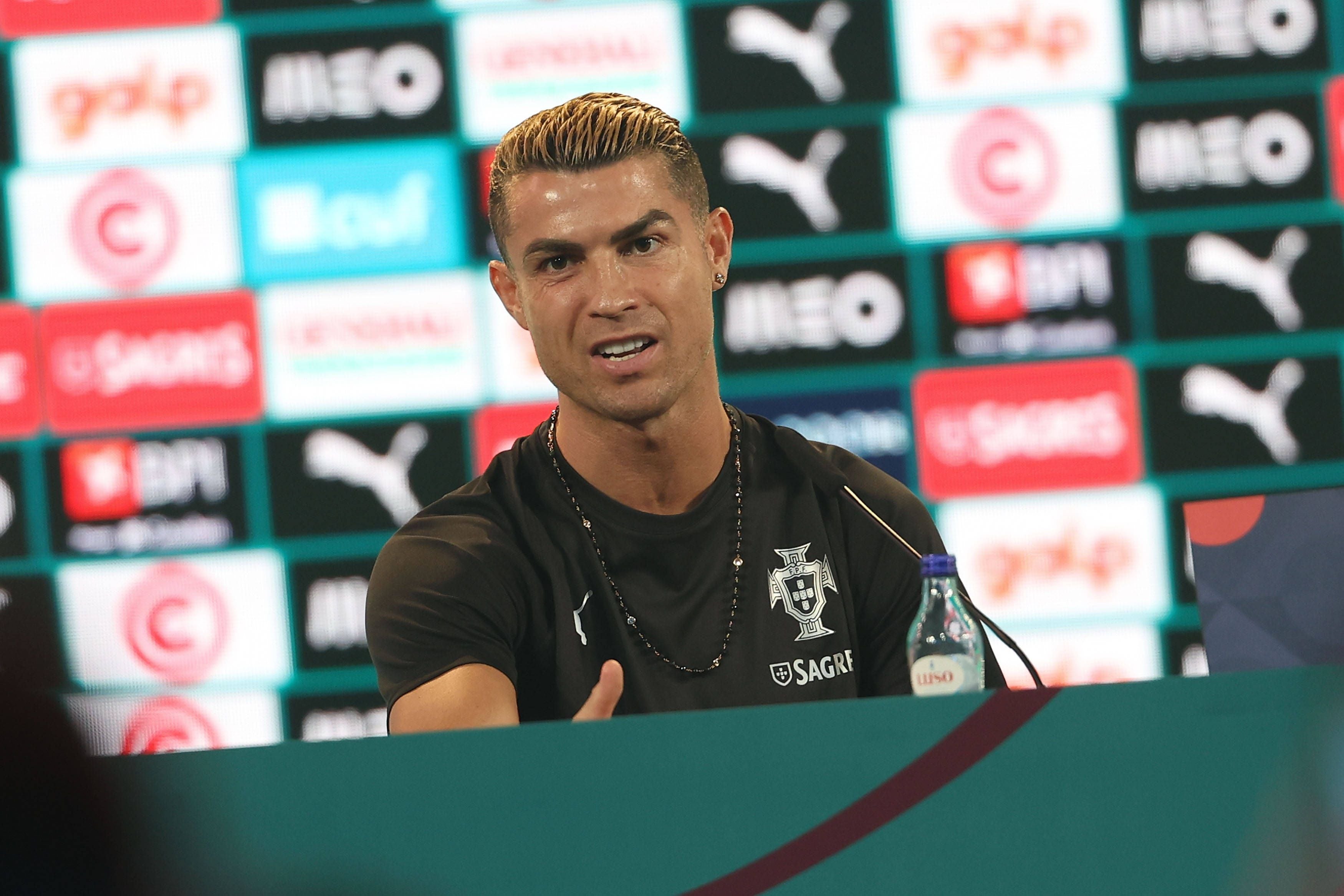 Cristiano Ronaldo sitzt bei einer Pressekonferenz im schwarzen Trikot der portugiesischen Nationalmannschaft und spricht in ein Mikrofon.