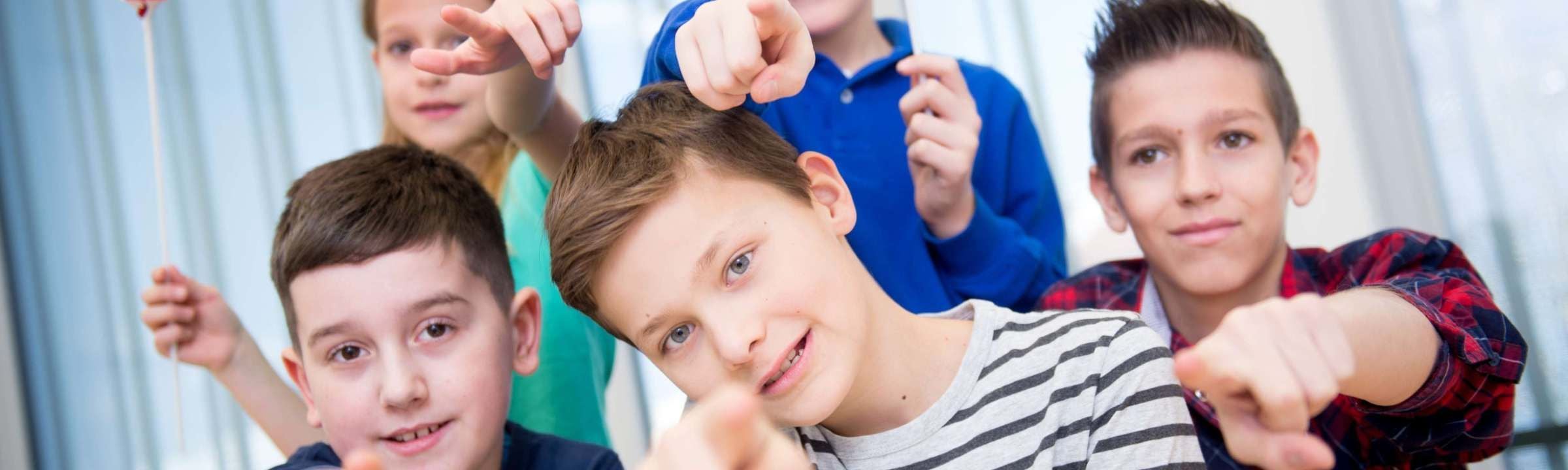 Fünf Kinder lächeln in die Kamera und zeigen mit den Fingern nach vorne.