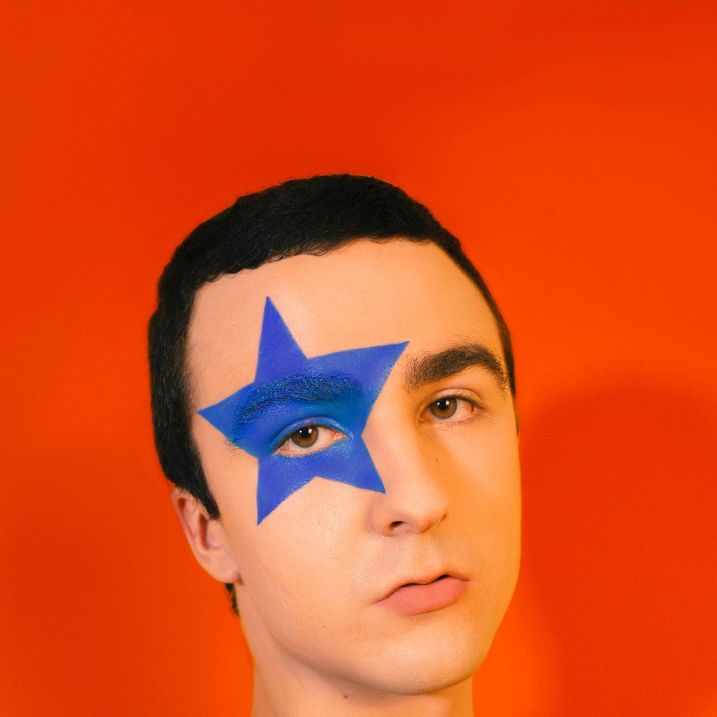 Person mit blauem Stern im Gesicht vor orangefarbenem Hintergrund.