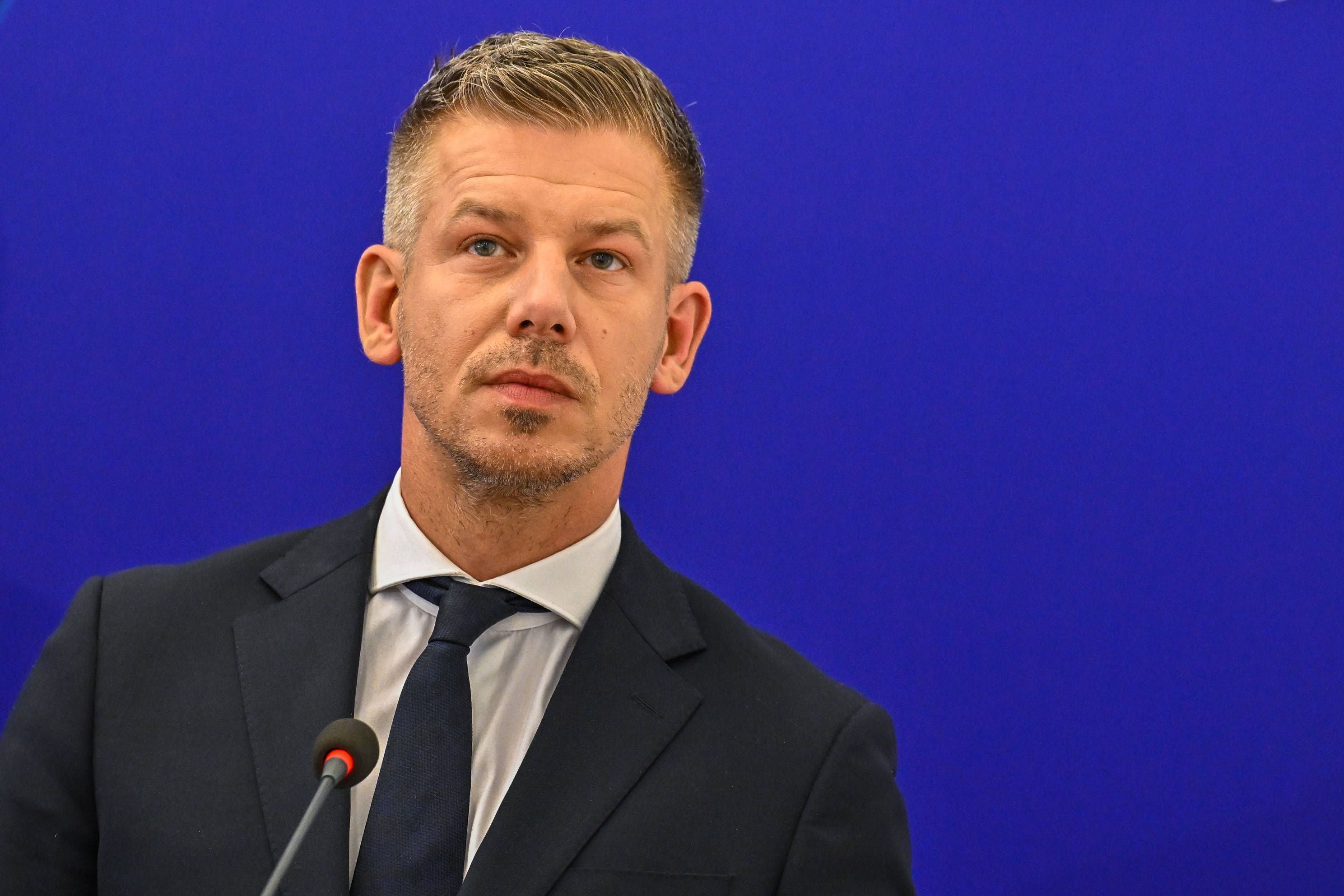 Ein Mann im Anzug spricht auf einer Pressekonferenz vor blauem Hintergrund ins Mikrofon.