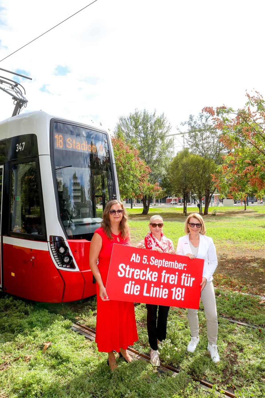 Drei Frauen stehen vor einer Straßenbahn mit einem Schild zur Freigabe der Linie 18 am 5. September.