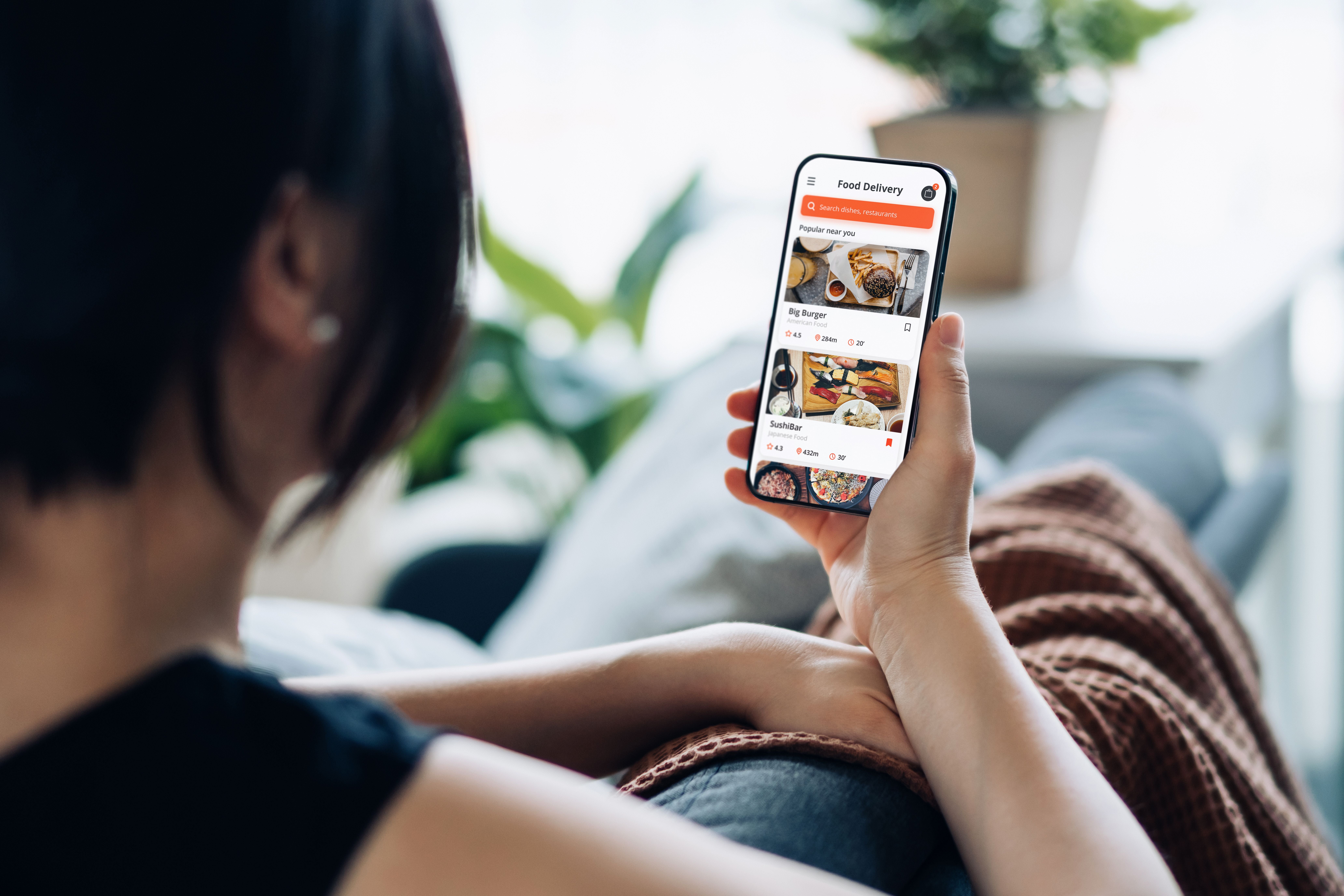 Frau liegt auf dem Sofa und bestellt Essen über eine Lieferdienst-App auf ihrem Smartphone.