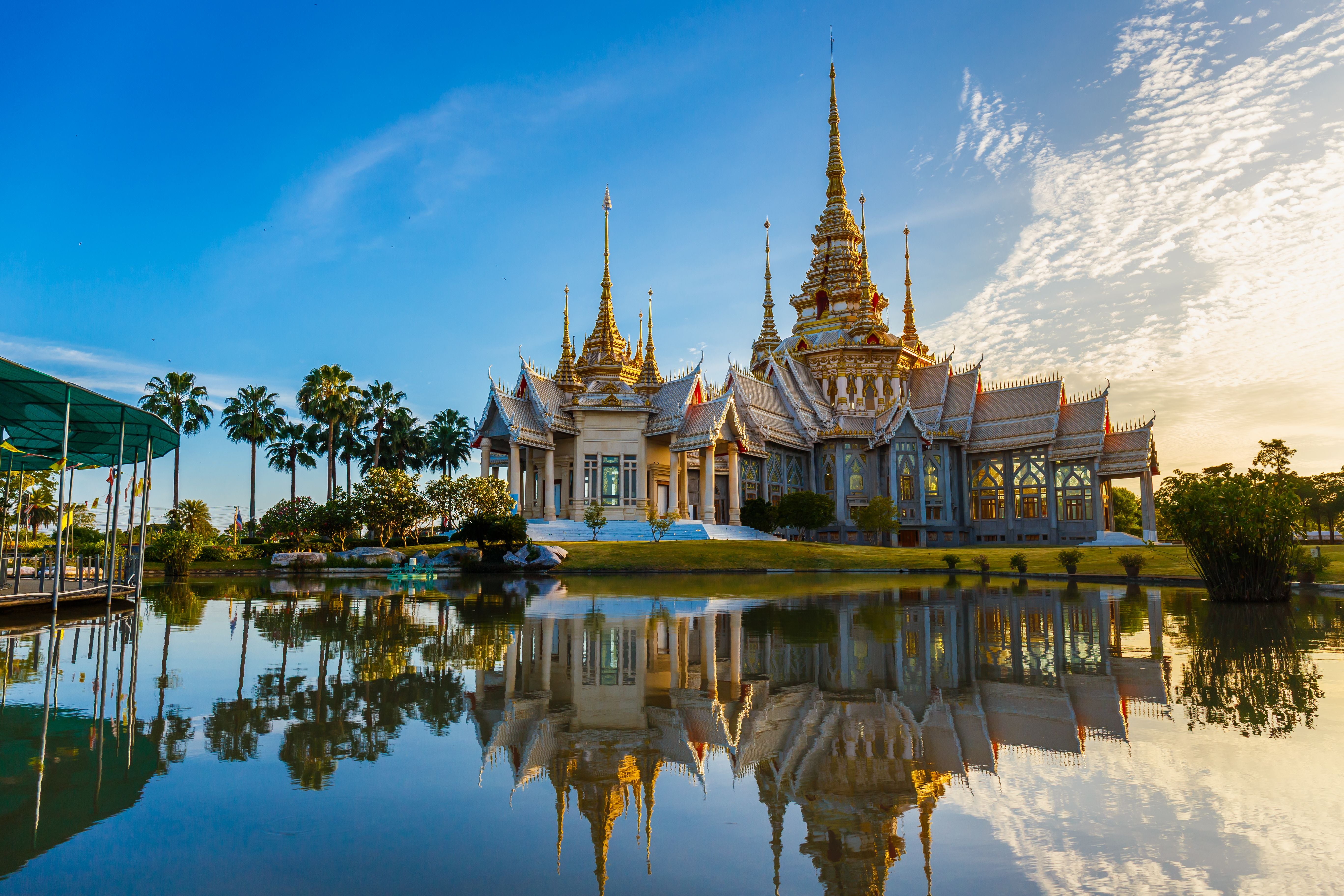Thailändischer Tempel Wat Non Kum spiegelt sich bei Sonnenuntergang im ruhigen Wasser wider.