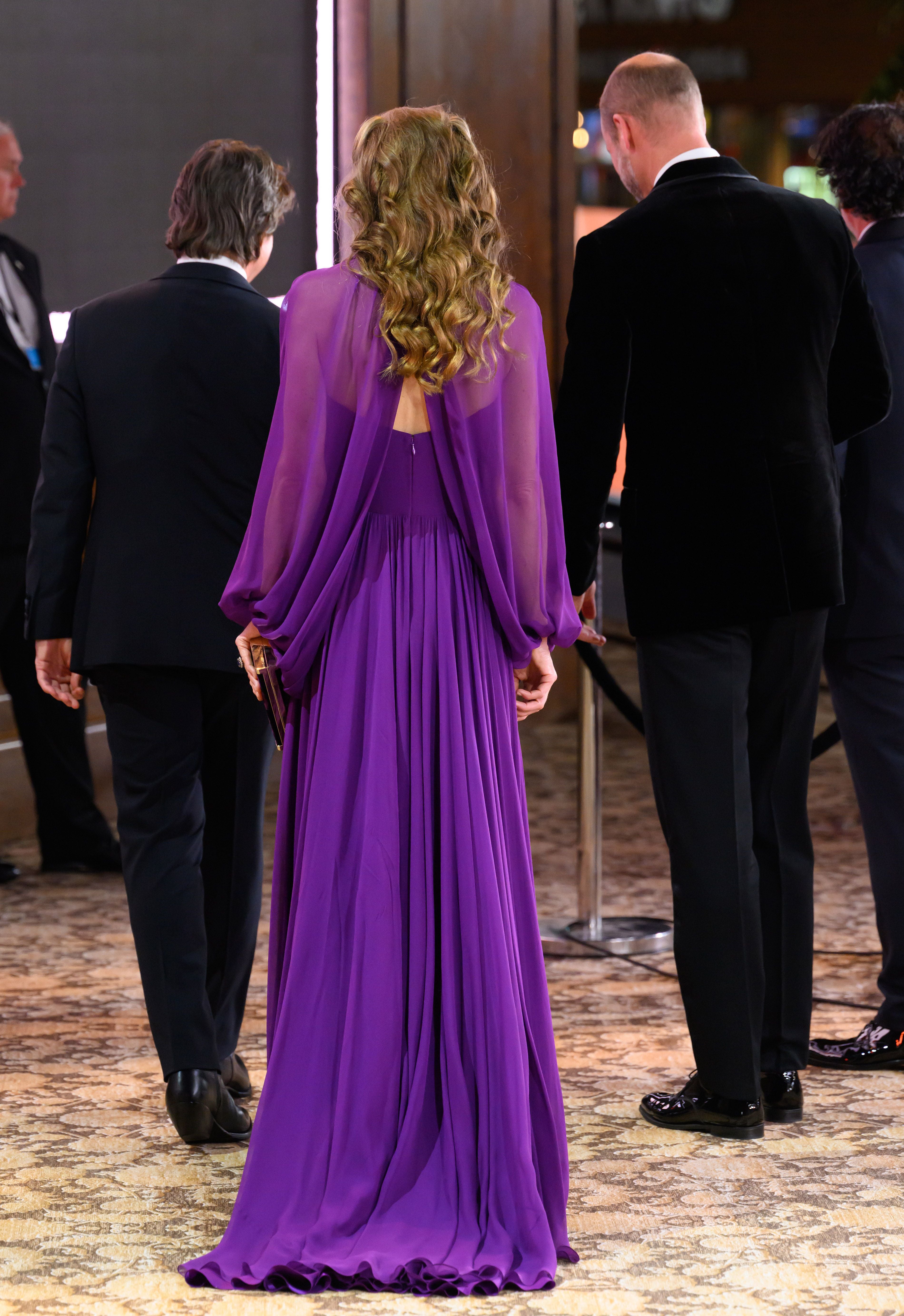 Frau im langen lila Kleid steht mit drei Männern im Anzug auf einem Event.