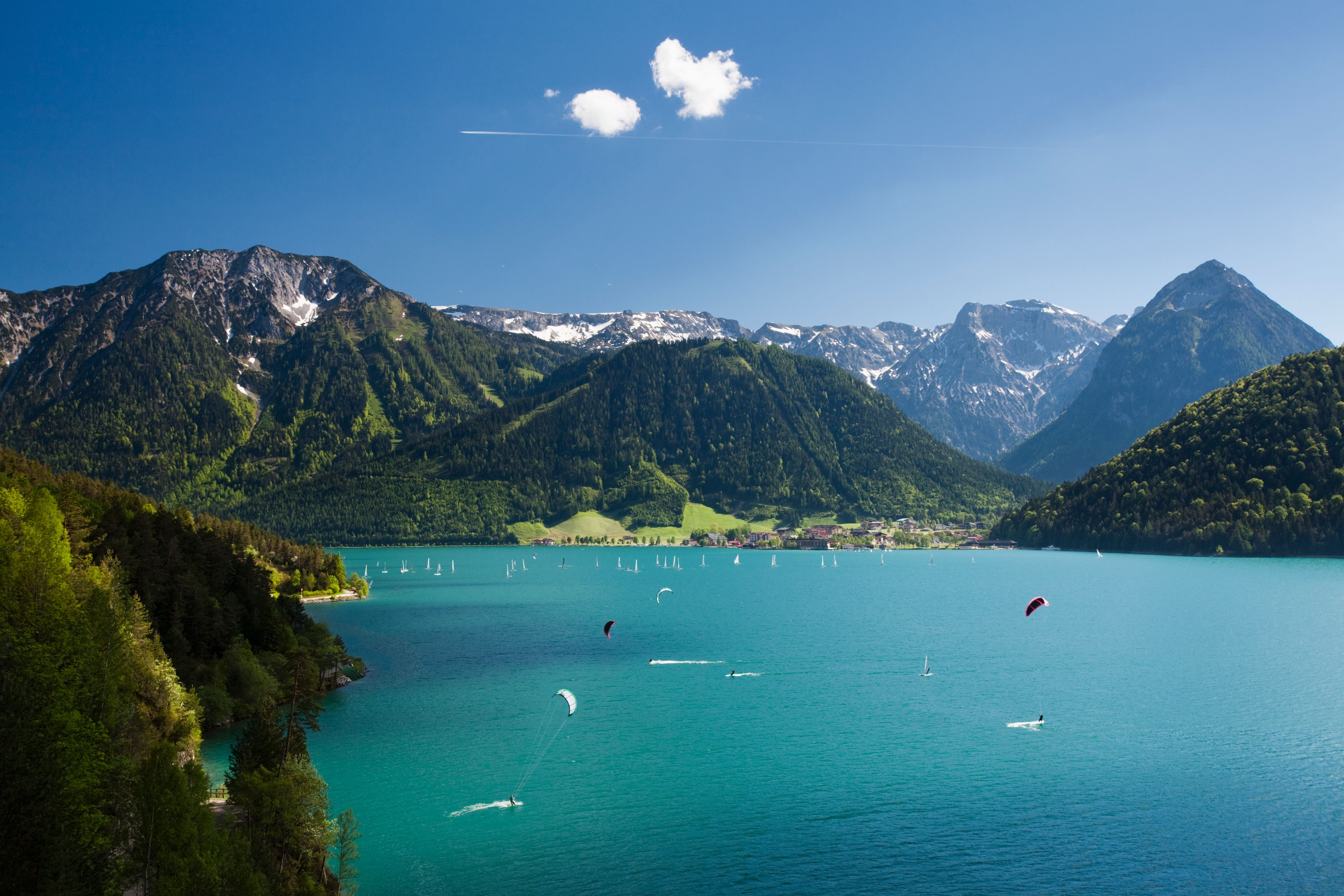 Türkisfarbener See in Tirol, umgeben von Bergen, mit Segel- und Kitesurfern auf dem Wasser.