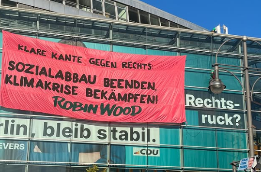 Großes Banner fordert soziale Gerechtigkeit und Klimaschutz vor einem CDU-Wahlplakat.