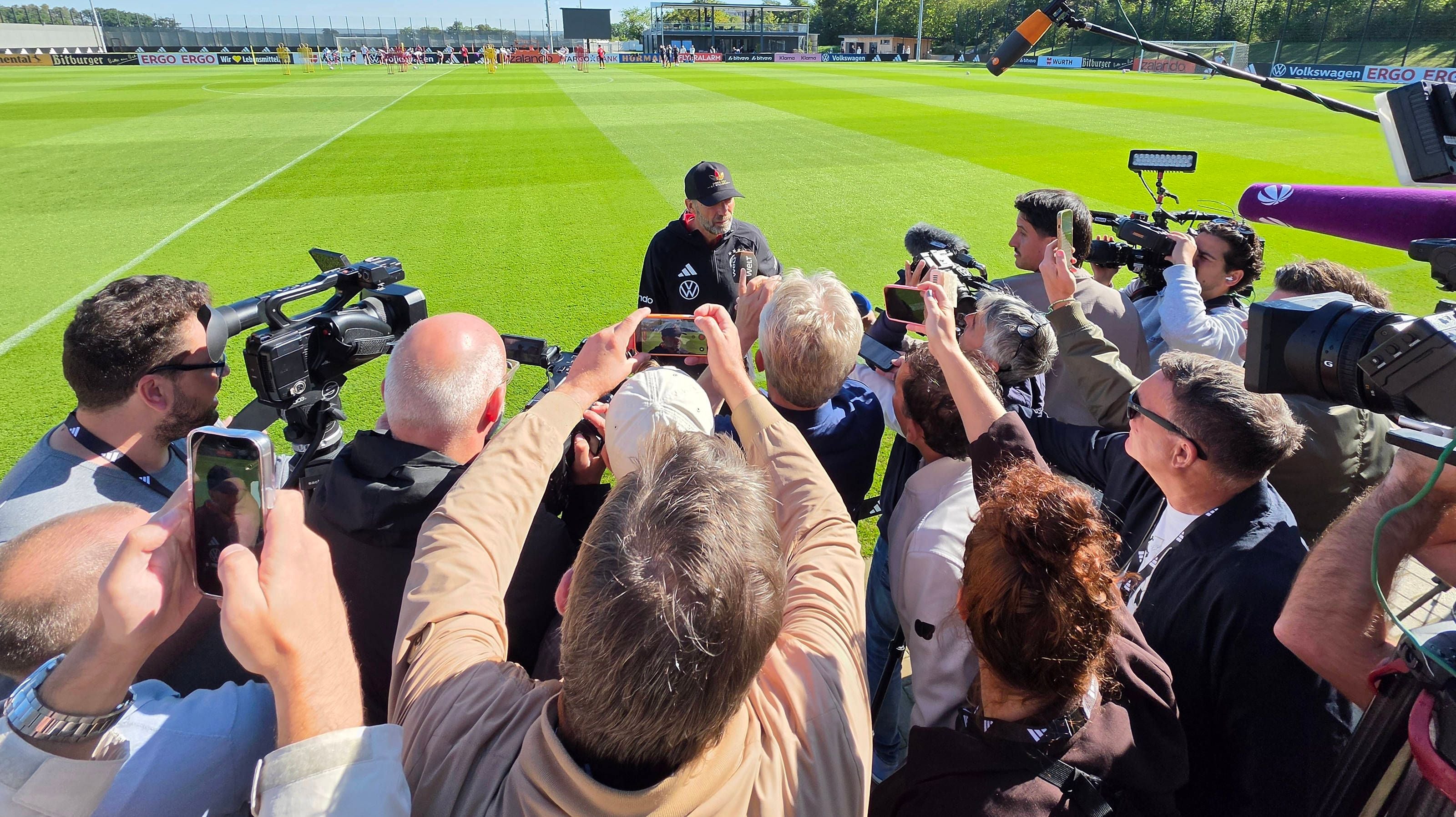 Jürgen Klopp steht im Zentrum einer großen Traube von Journalisten, Fotografen und Kameraleuten auf dem Trainingsplatz.