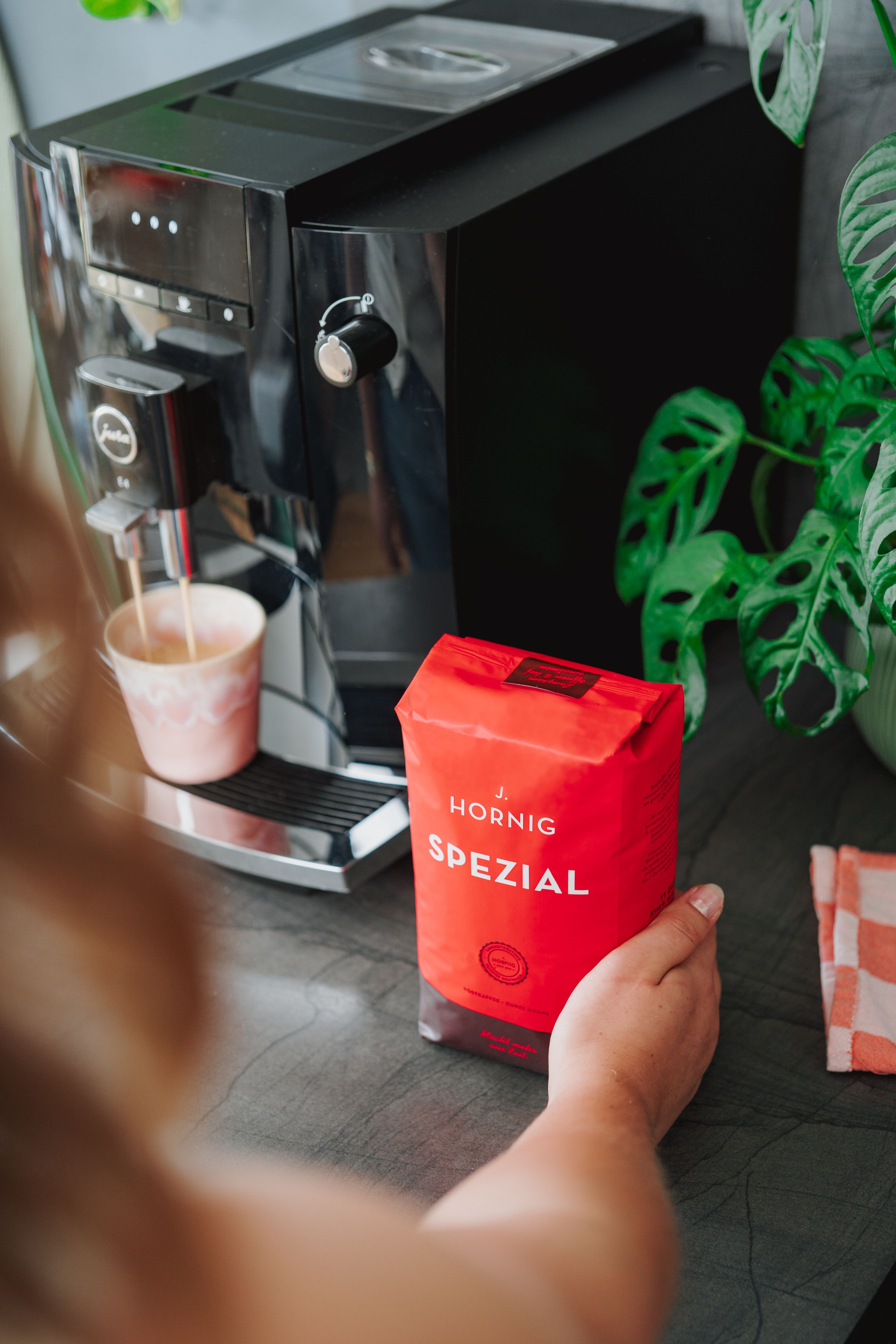 Eine Person hält J. Hornig Spezial Kaffee vor einem Kaffeevollautomaten.