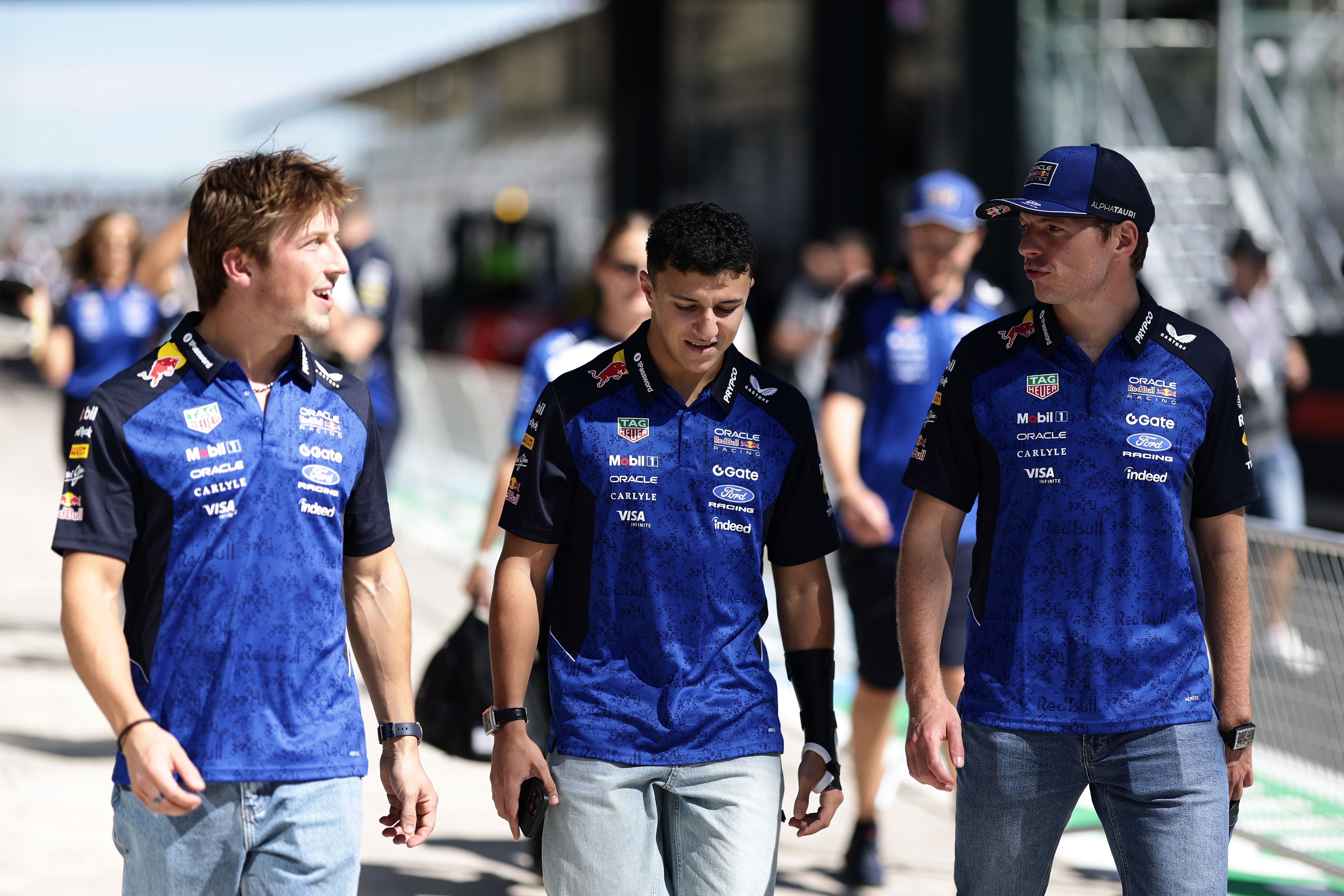 Drei Männer im Red Bull Racing Team-Outfit gehen nebeneinander in einer Boxengasse.