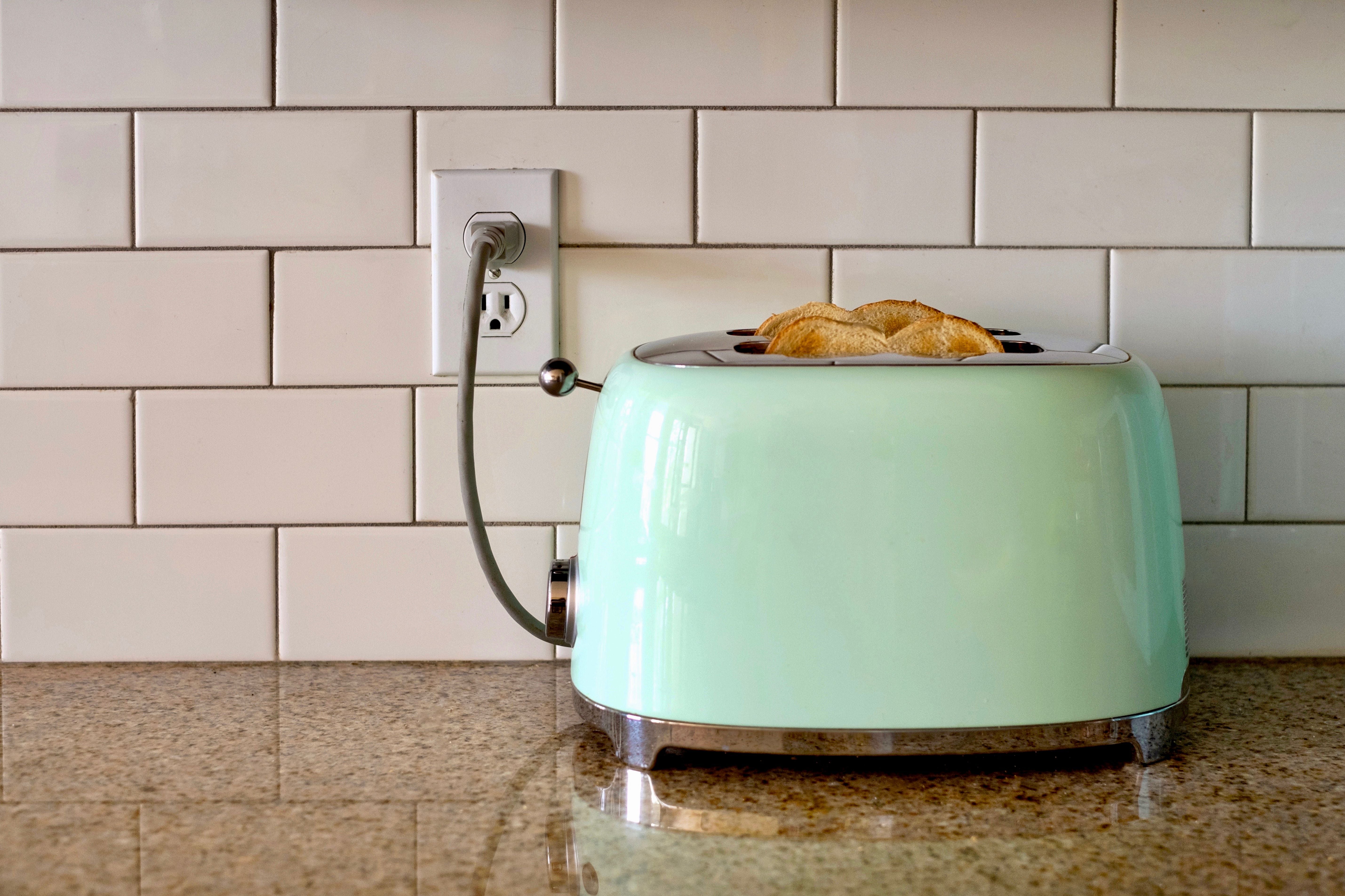 Hellgrüner Toaster mit Toastscheiben steht auf einer Küchenarbeitsplatte vor weißen Fliesen.