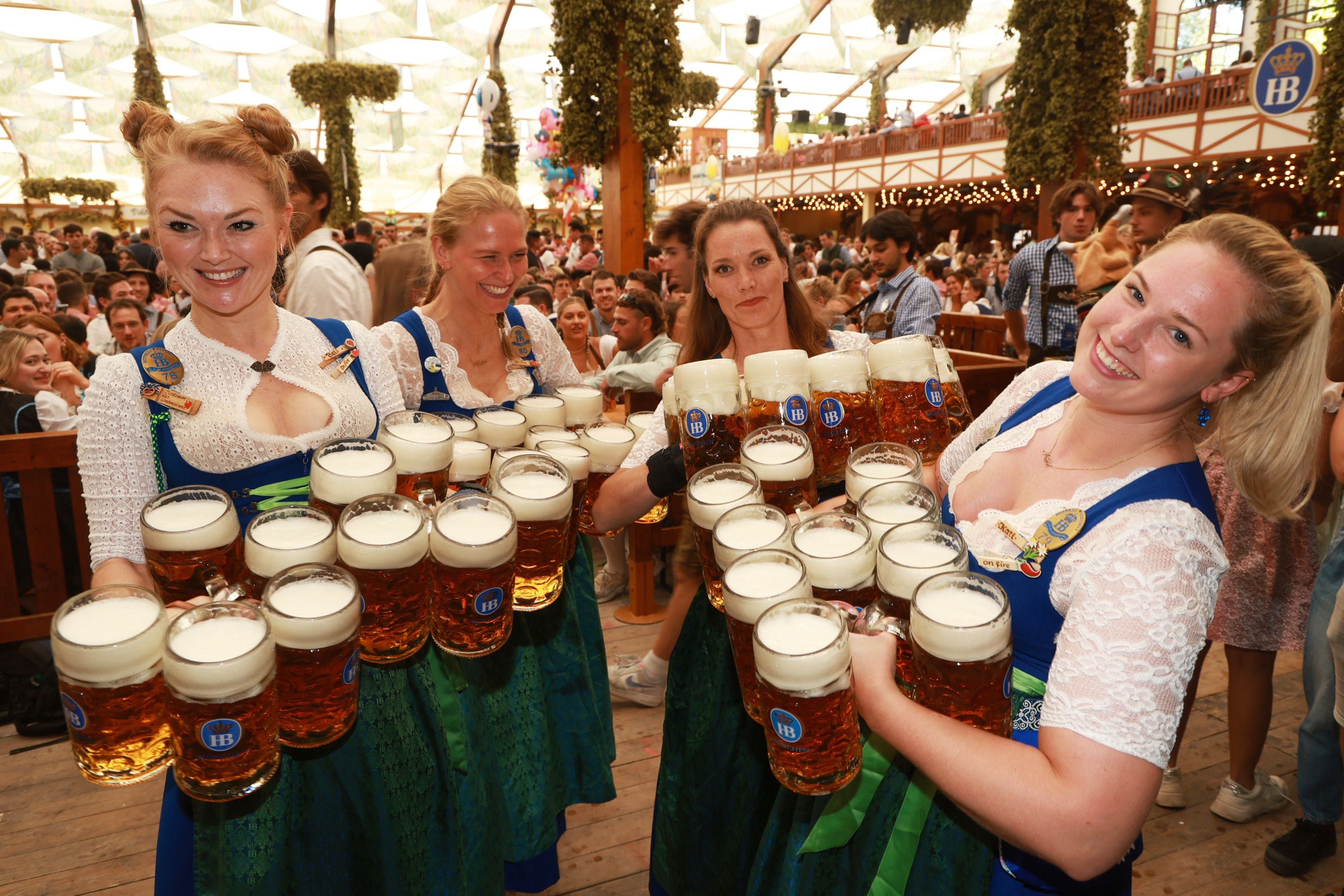 Vier Bedienungen tragen zahlreiche Maß Bier auf dem Oktoberfest in einem voll besetzten Festzelt.