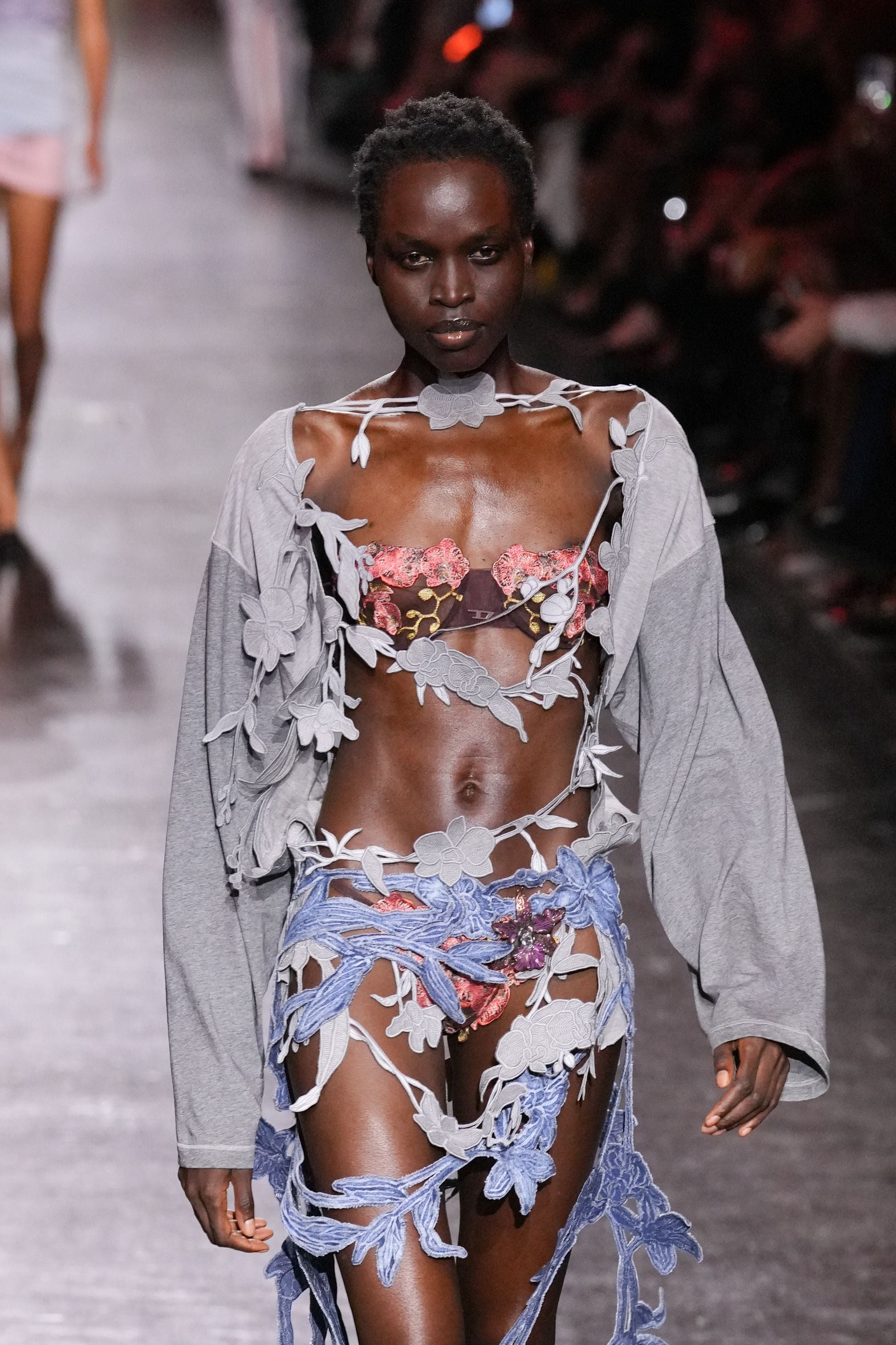 Model trägt ausgefallene Blumenmode mit grauer Jacke auf dem Laufsteg der Milan Fashion Week.