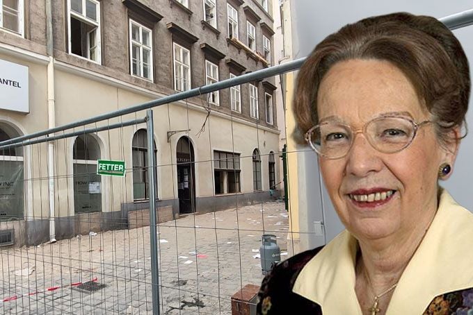 Ältere Frau mit Brille vor abgesperrtem, beschädigtem Gebäude nach Hauseinsturz.