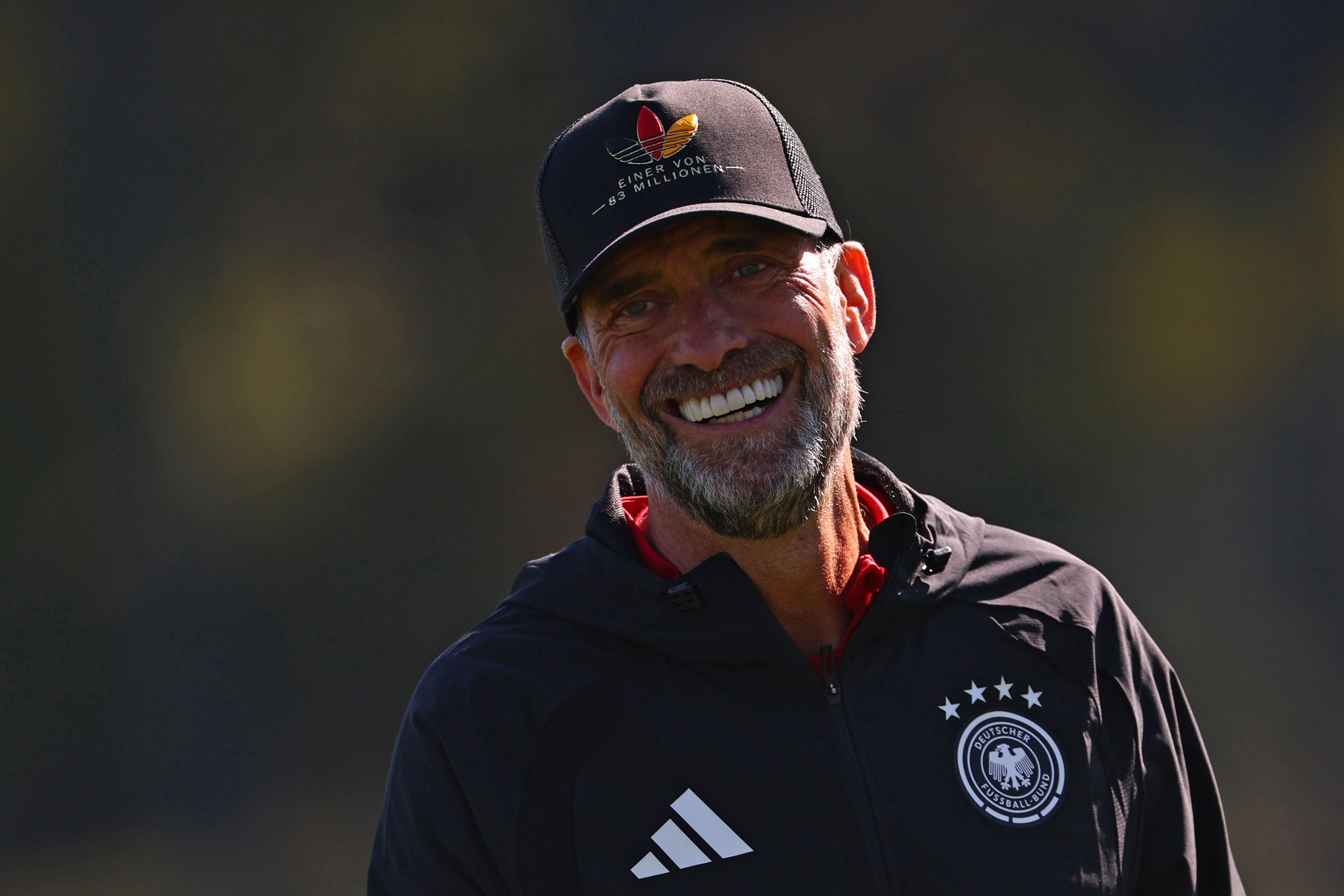 Ein lächelnder Mann in Trainingsjacke des DFB steht im Freien und trägt eine schwarze Kappe.