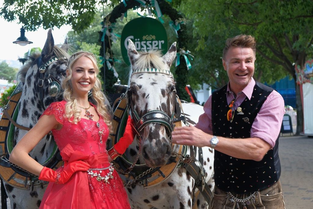 Eine Frau und ein Mann in Tracht posieren mit zwei gescheckten Pferden auf einem Fest.