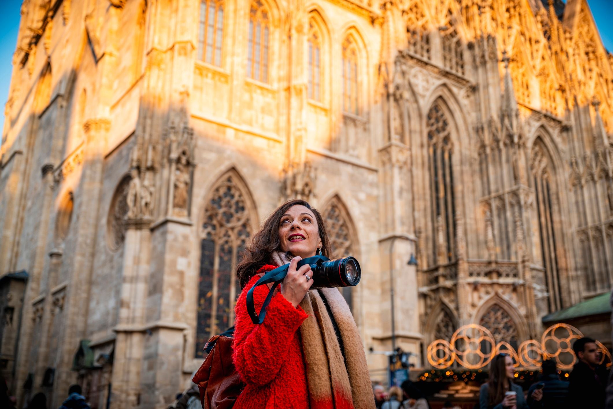 Frau mit Kamera und rotem Mantel vor dem Stephansdom in Wien bei Sonnenlicht.