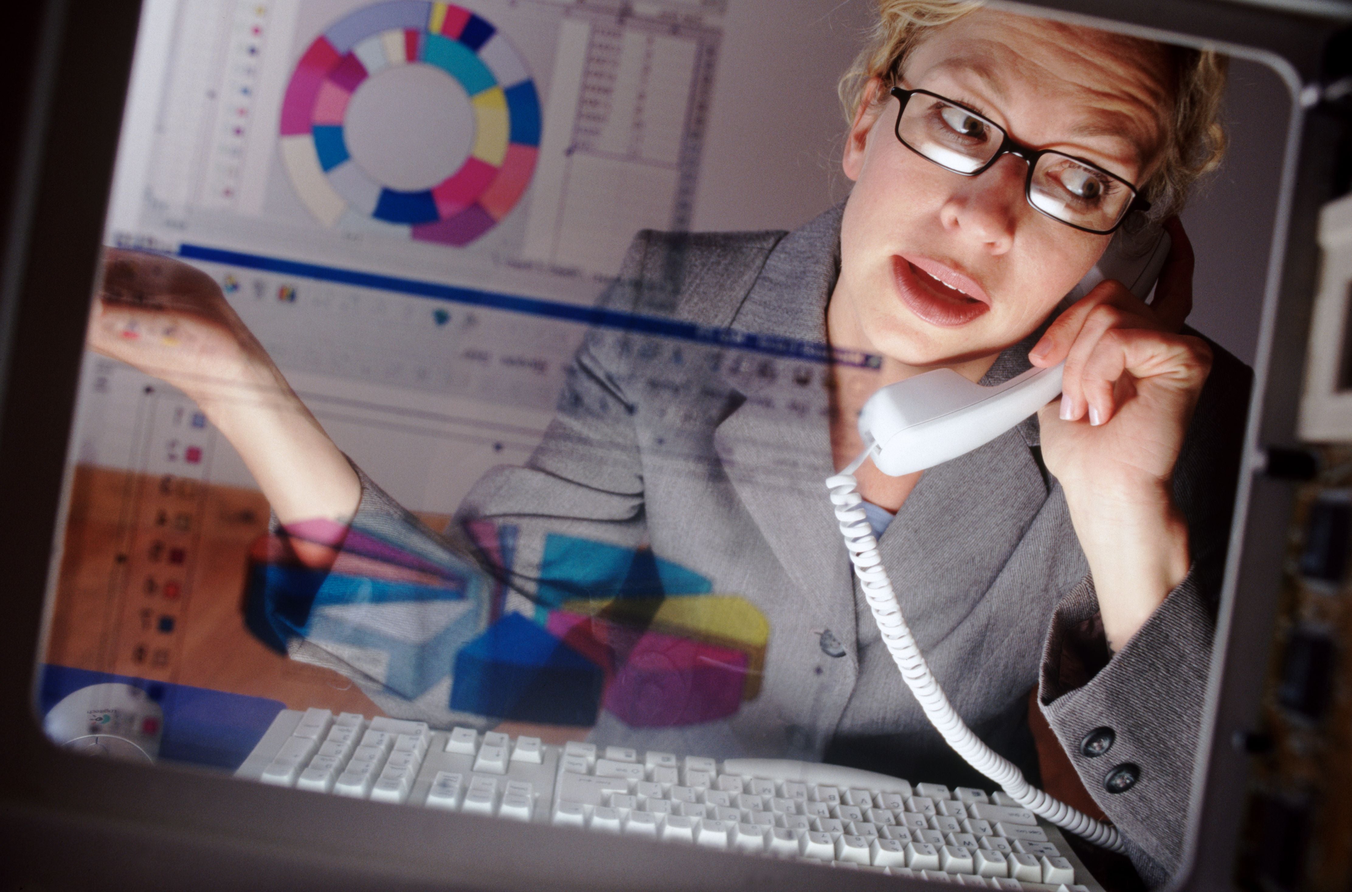 Frau telefoniert am Schreibtisch vor einem Computer mit Diagrammen auf dem Bildschirm.