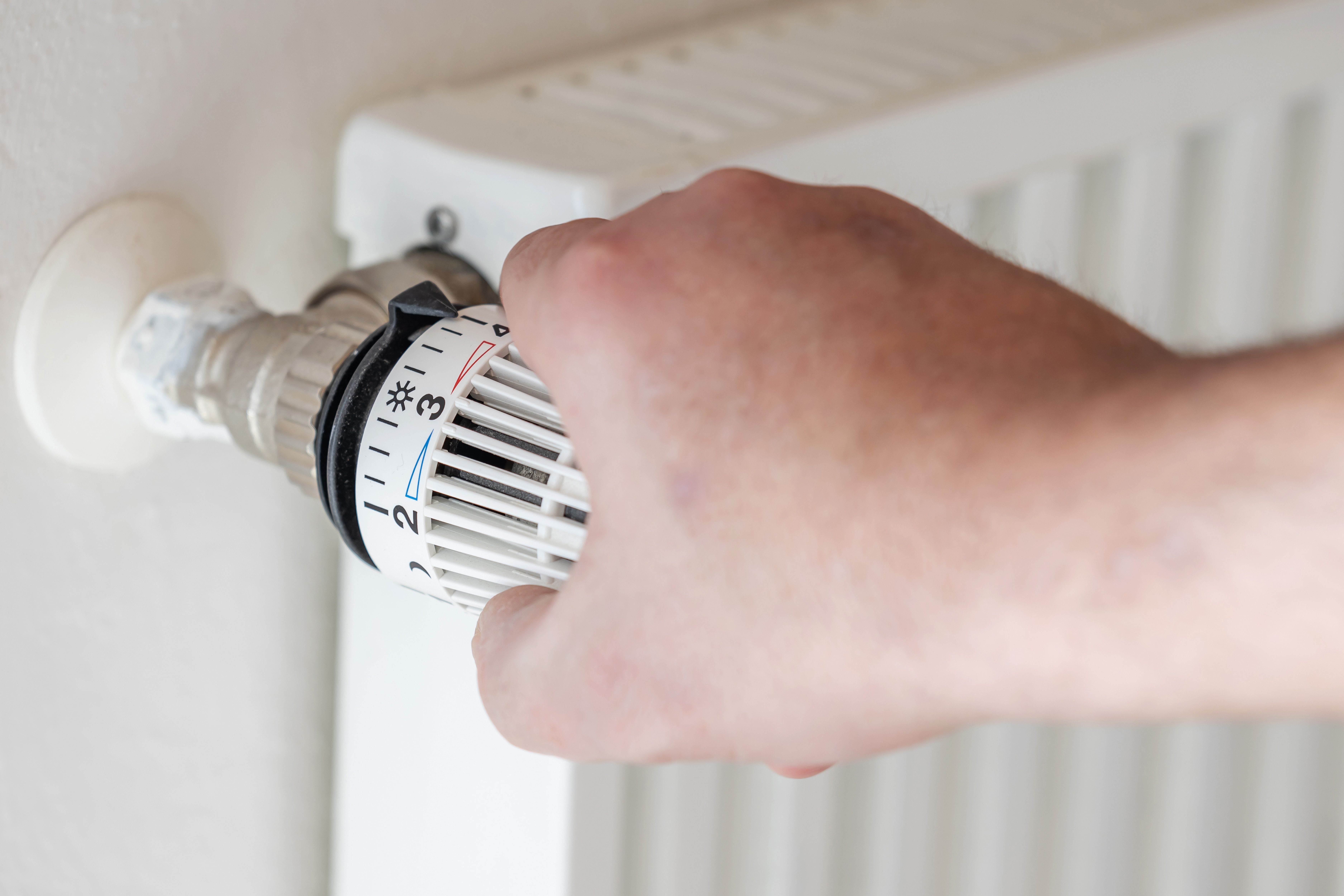 Eine Hand dreht am Thermostat eines Heizkörpers.