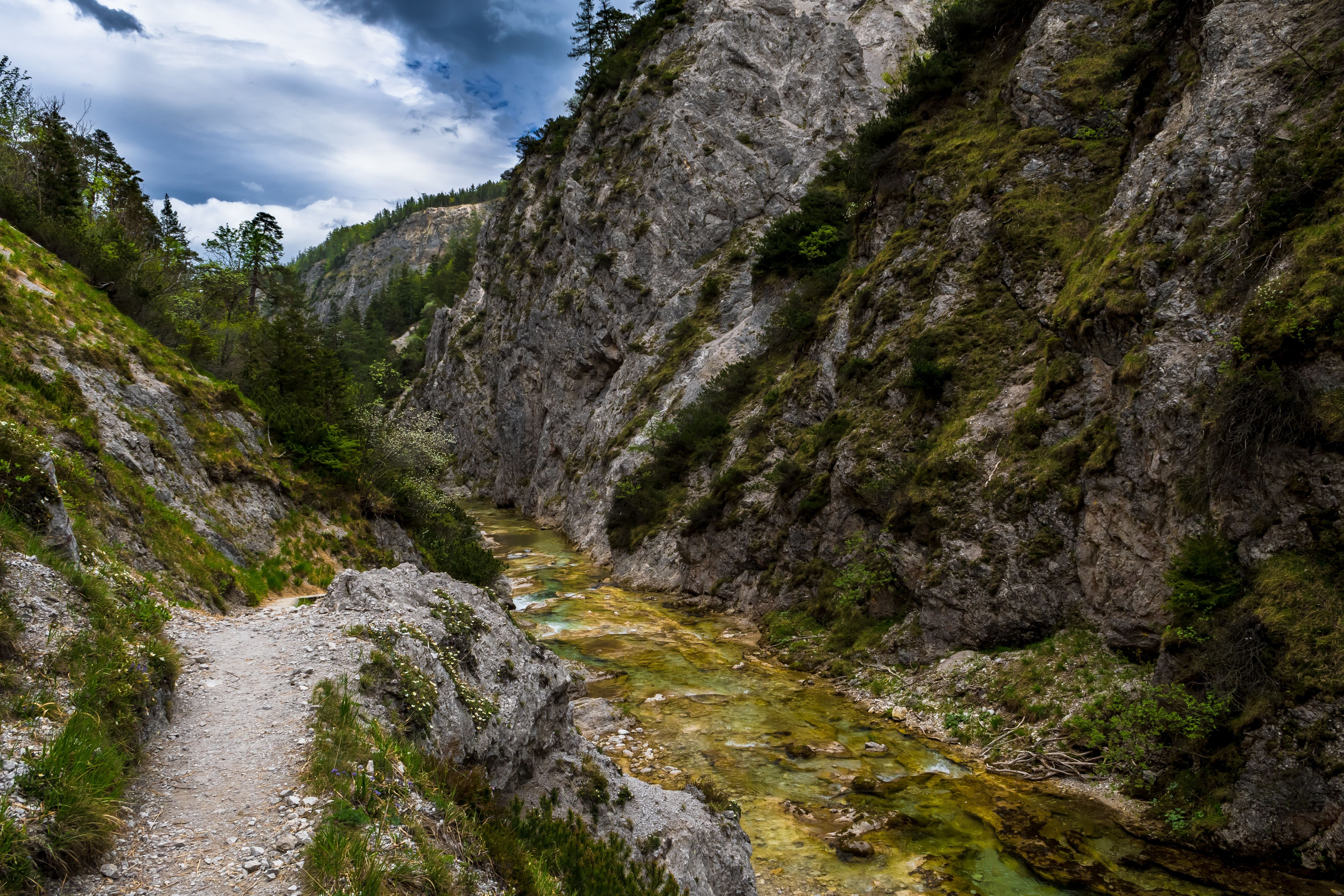 Schmaler Wanderweg entlang eines klaren Bergflusses in einer steilen Felsenschlucht in Österreich.
