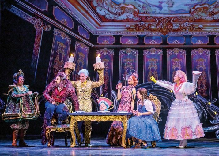 Kostümierte Schauspieler spielen eine Szene aus „Die Schöne und das Biest“ auf der Theaterbühne.