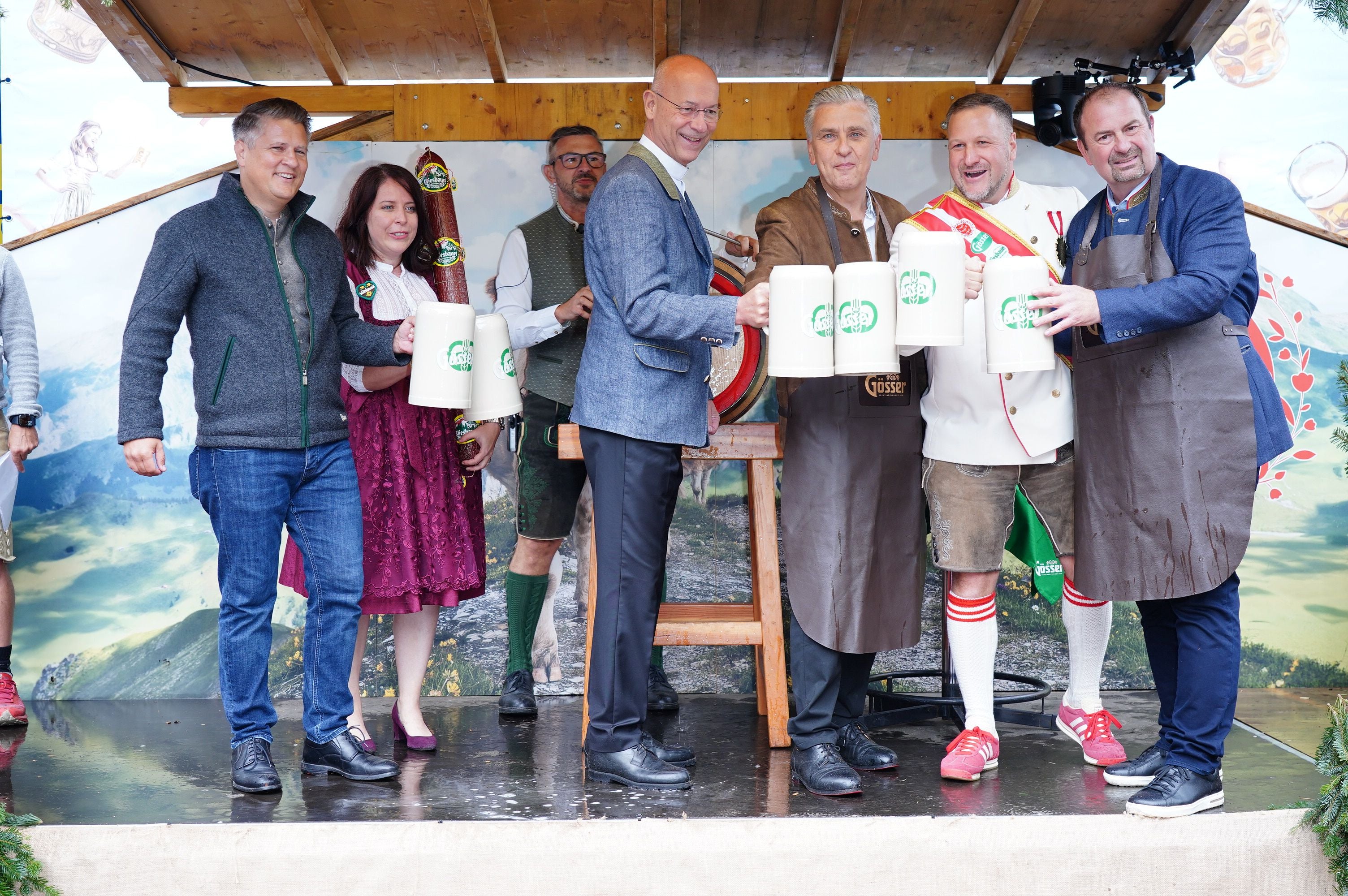 Gruppe feiert den Bieranstich auf der Wiener Kaiser Wiesn mit Bierkrügen auf einer Bühne.