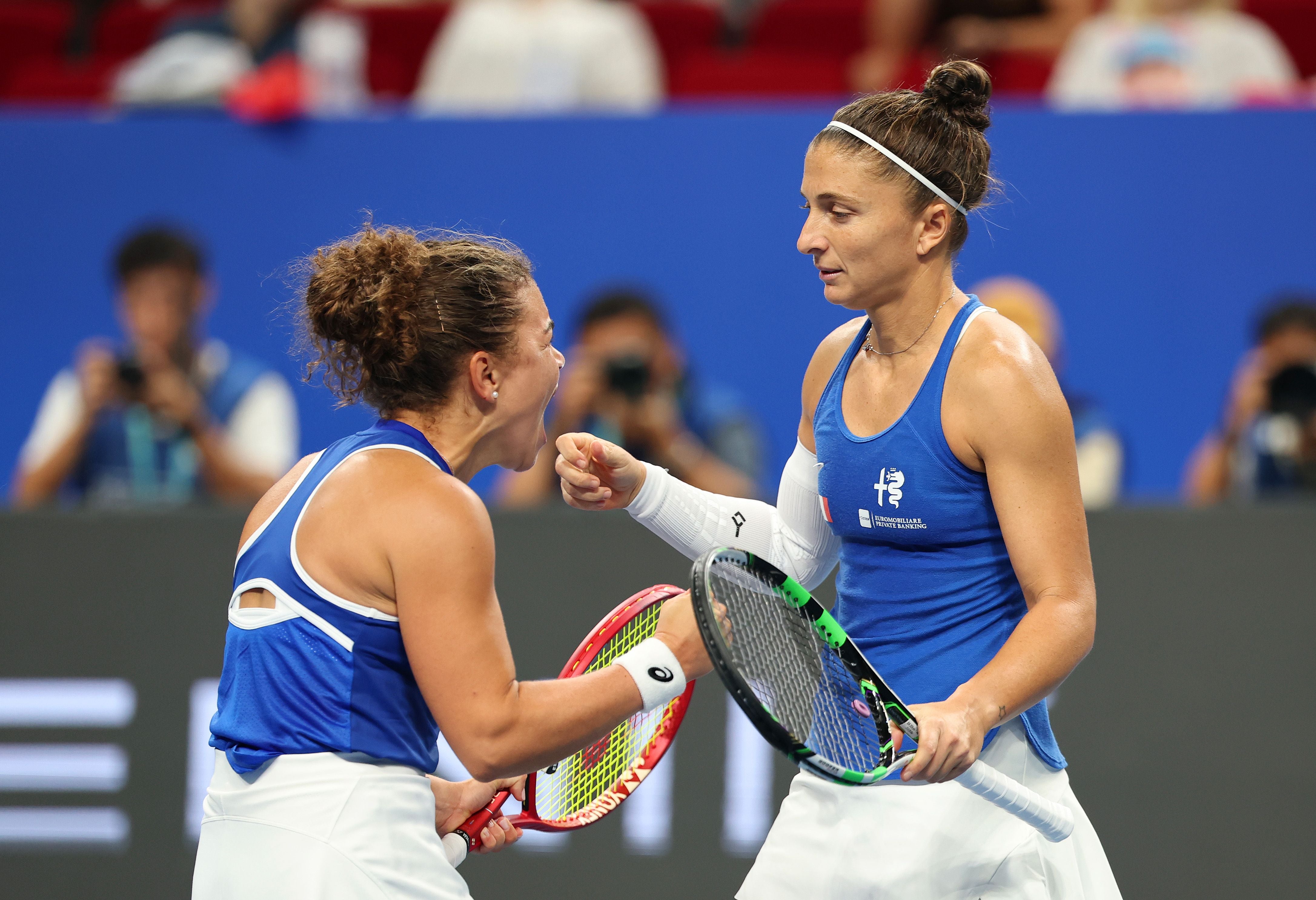Jasmine Paolini und Sara Errani jubeln im blauen Italien-Trikot auf dem Tennisplatz.
