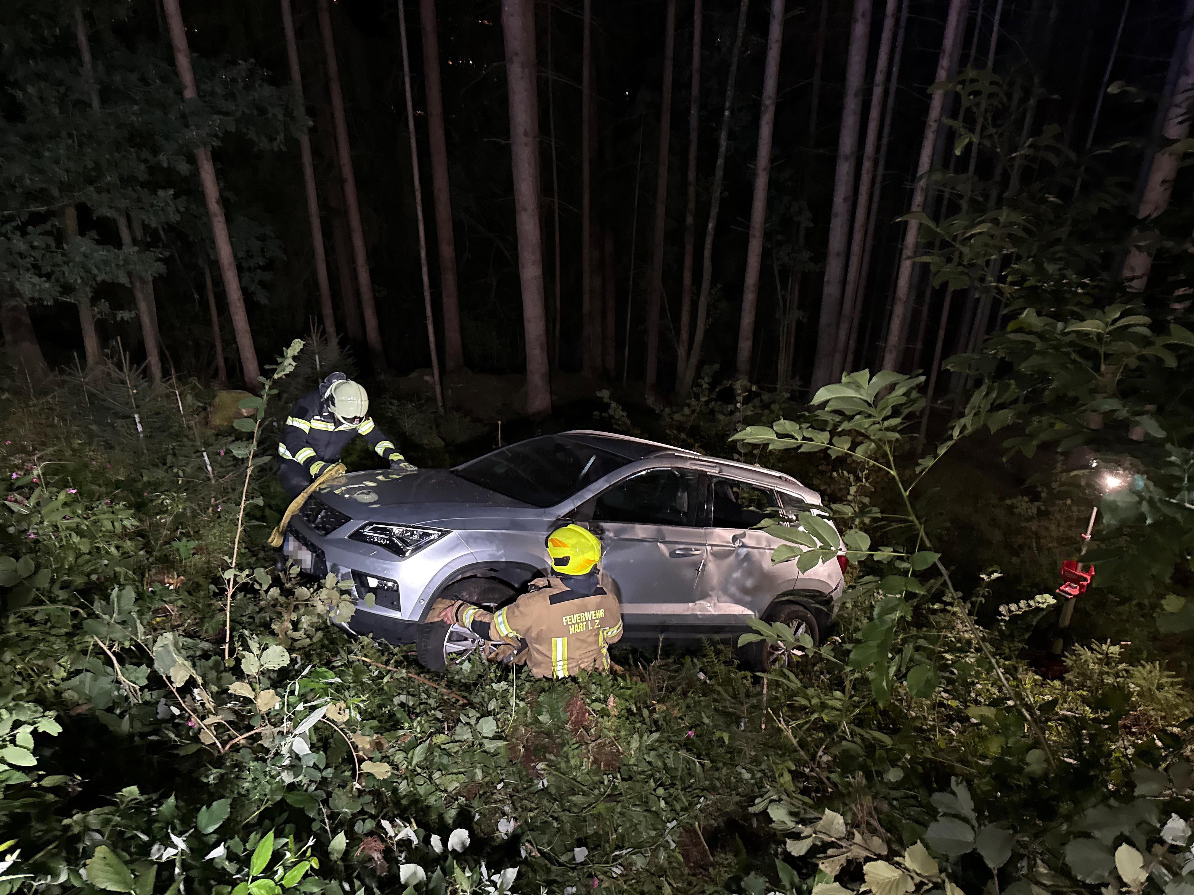 Zwei Feuerwehrleute sichern nachts ein verunfalltes Auto im Wald.