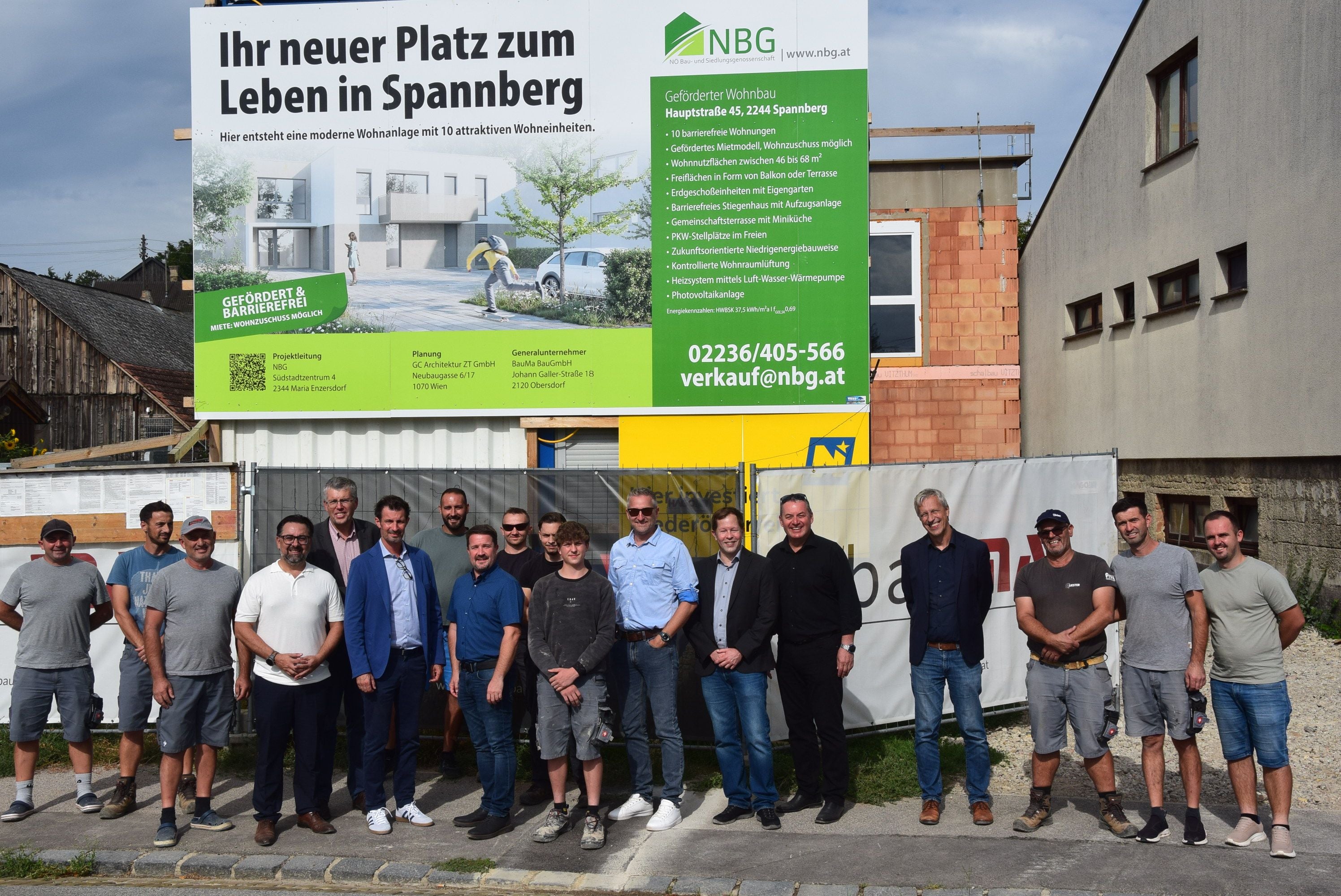 Gruppe von Menschen steht vor einer Baustelle mit einem großen Werbeschild für neue Wohnungen.