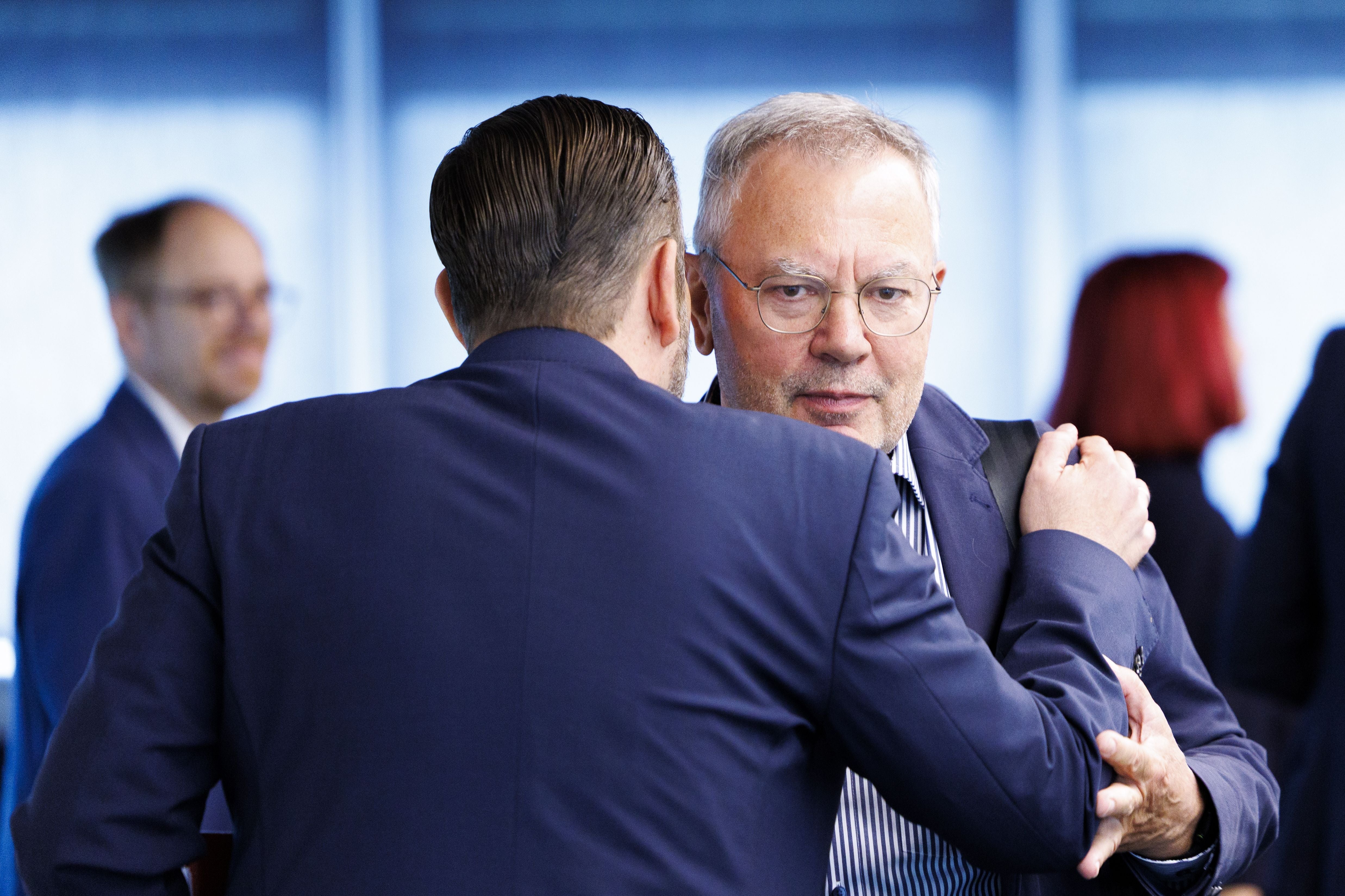 Zwei Männer in Anzügen begrüßen sich herzlich bei einer Veranstaltung.
