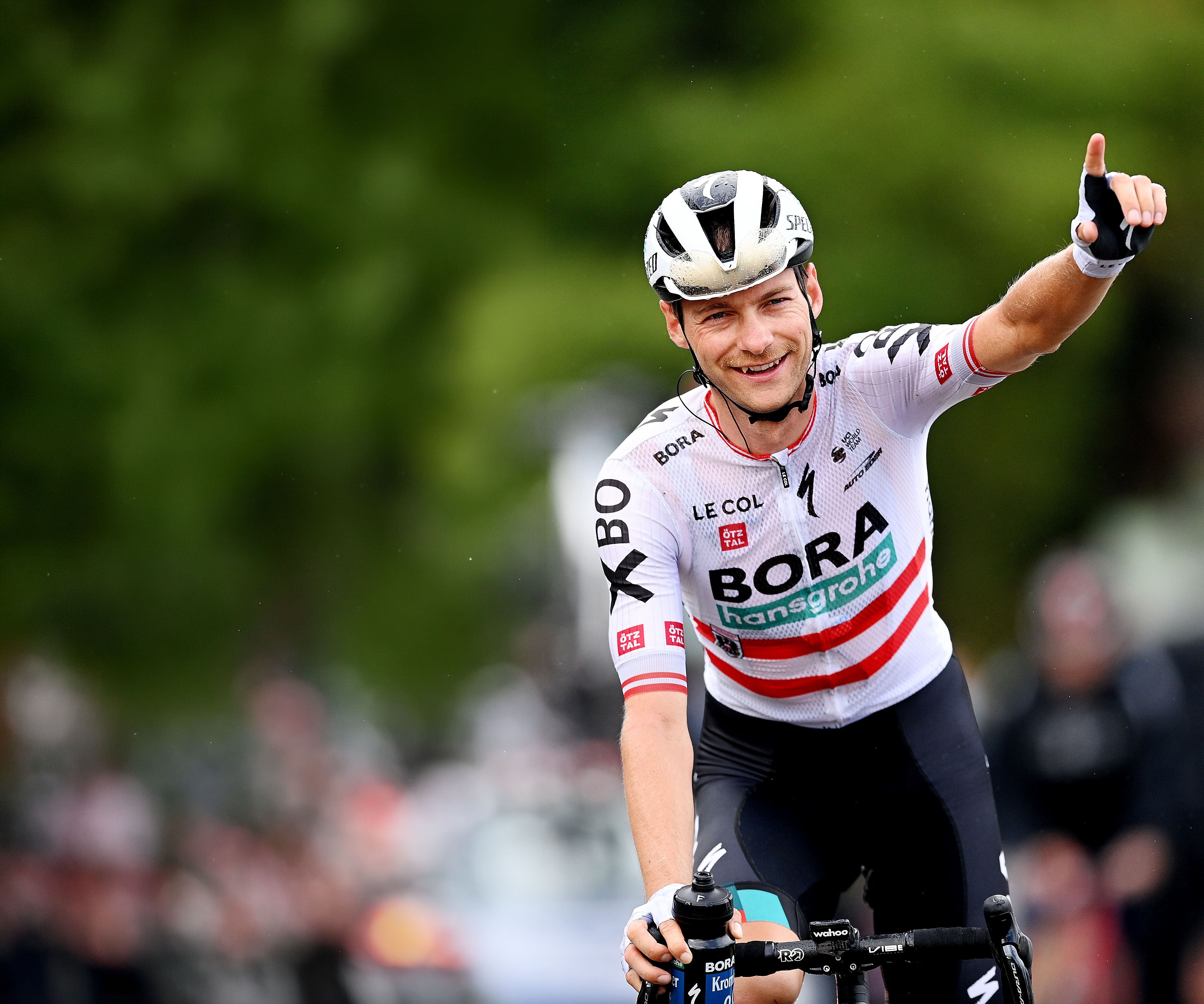Felix Großschartner streckt auf dem Rennrad den Daumen nach oben und lächelt.