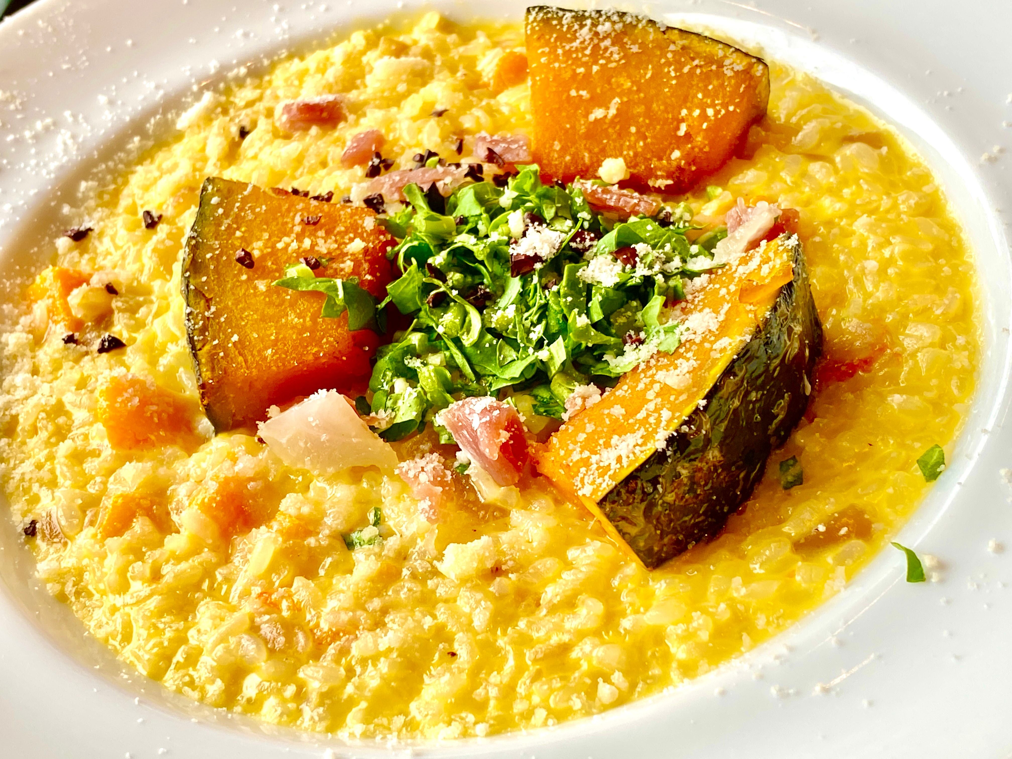 Cremiges Kürbisrisotto mit gebackenen Kürbisstücken, Kräutern und Schinken, garniert mit Parmesan.