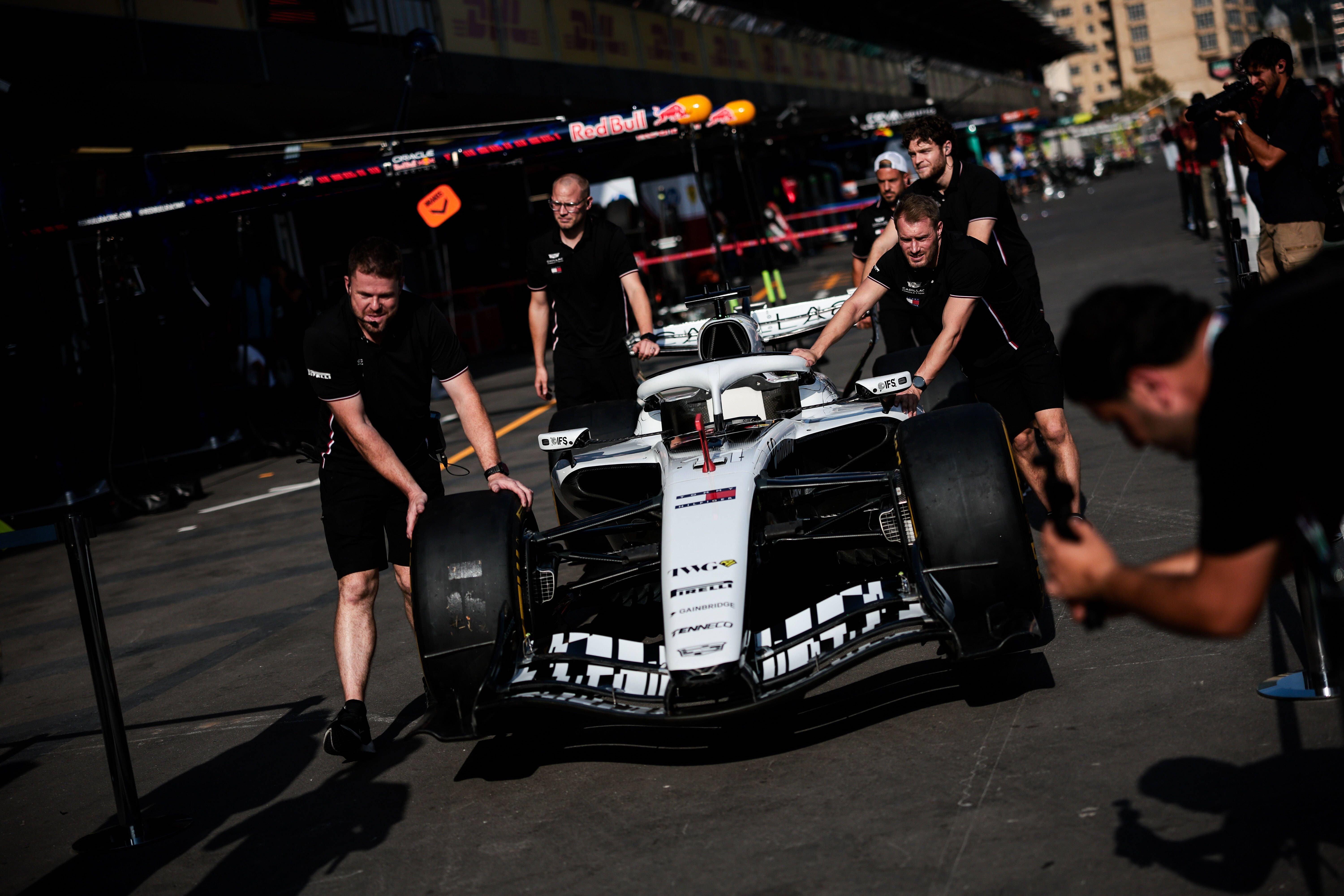 Mehrere Teammitglieder schieben einen Formel-1-Rennwagen durch die Boxengasse auf einer Rennstrecke.