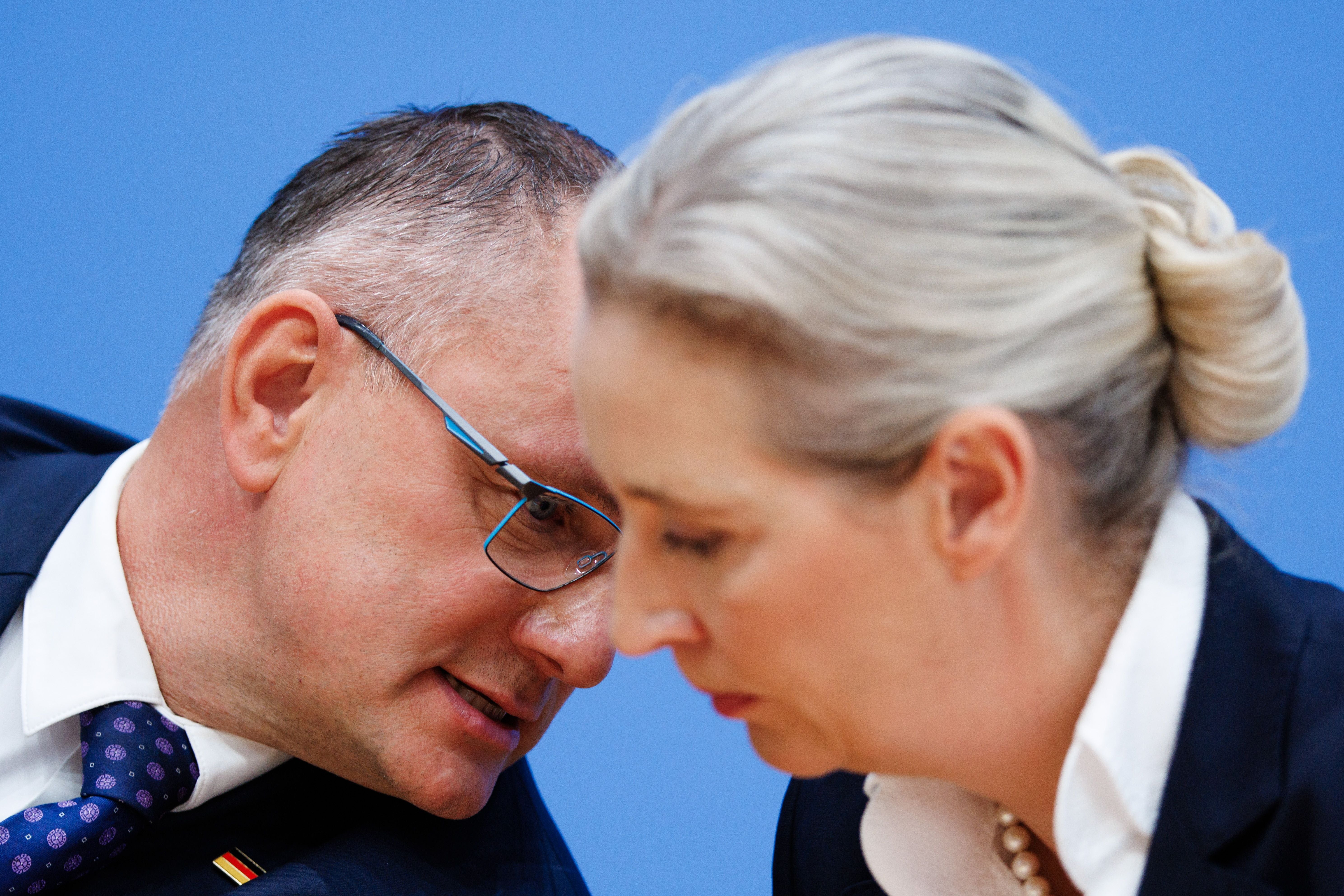 Ein Mann flüstert einer Frau auf einer Pressekonferenz etwas ins Ohr.
