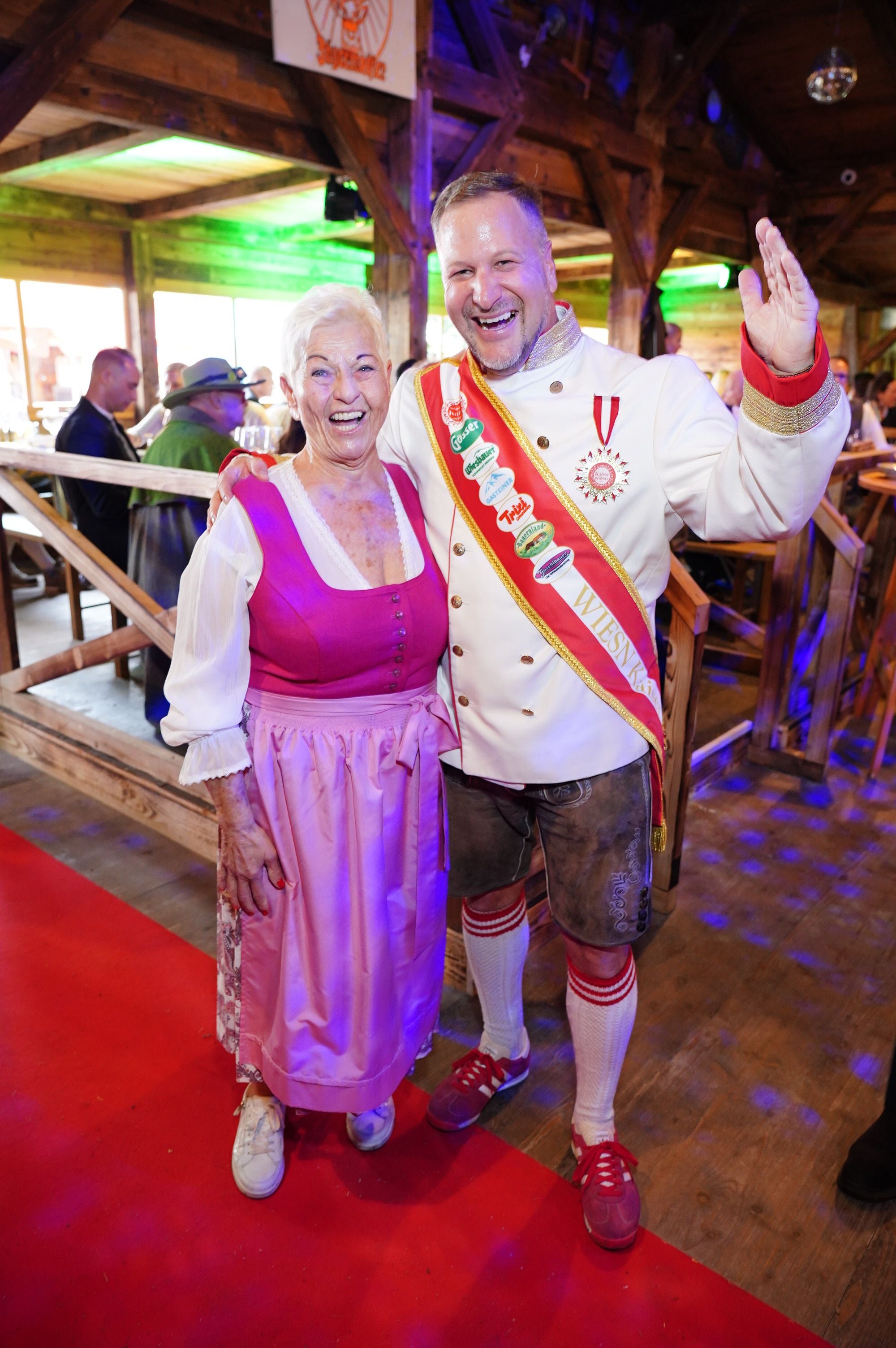 Zwei fröhliche Menschen in Tracht auf der Wiener Kaiser Wiesn posieren gemeinsam für ein Foto.