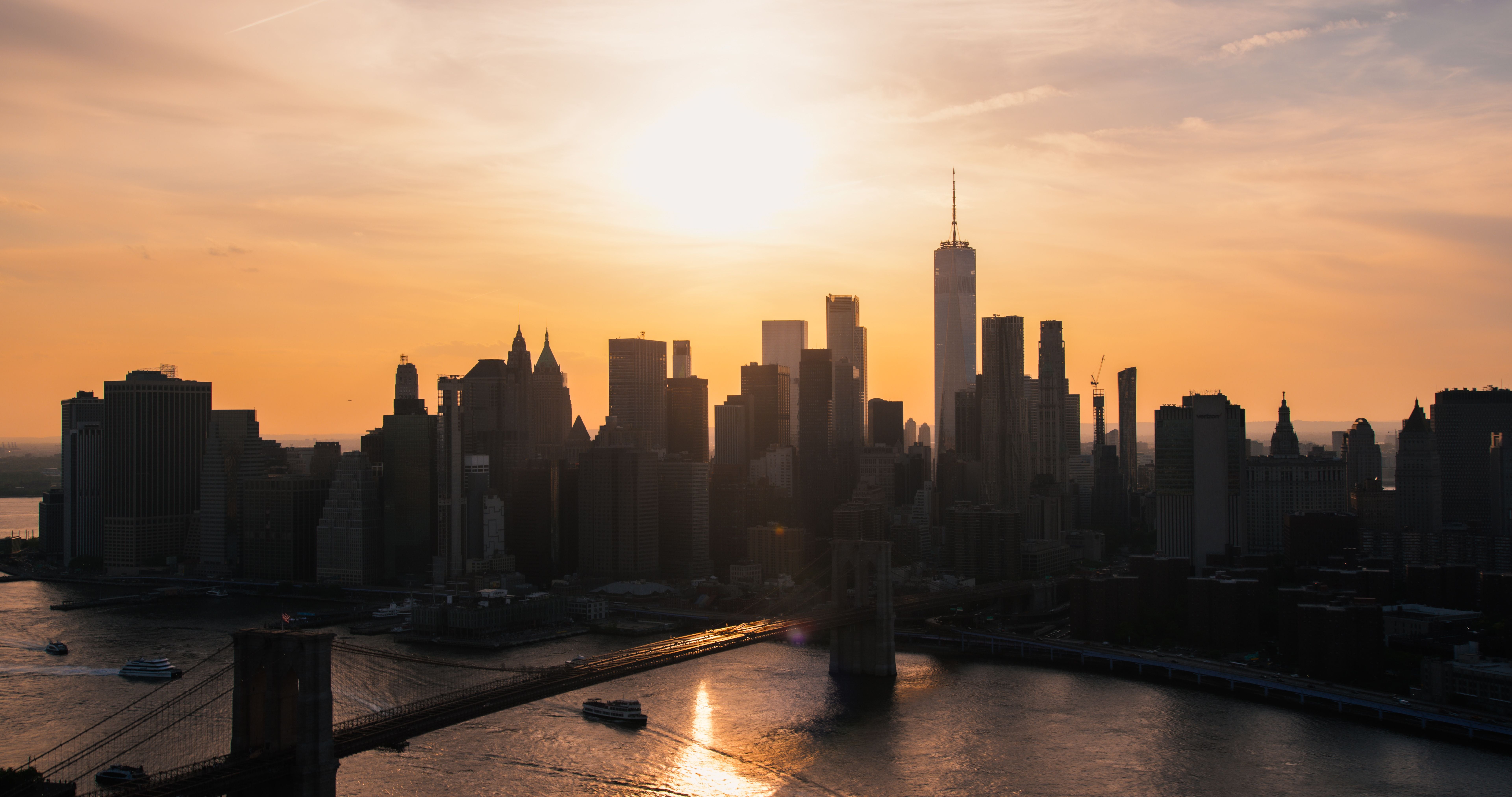 New Yorker Skyline mit Brooklyn Bridge und Fähren bei Sonnenuntergang über dem East River.