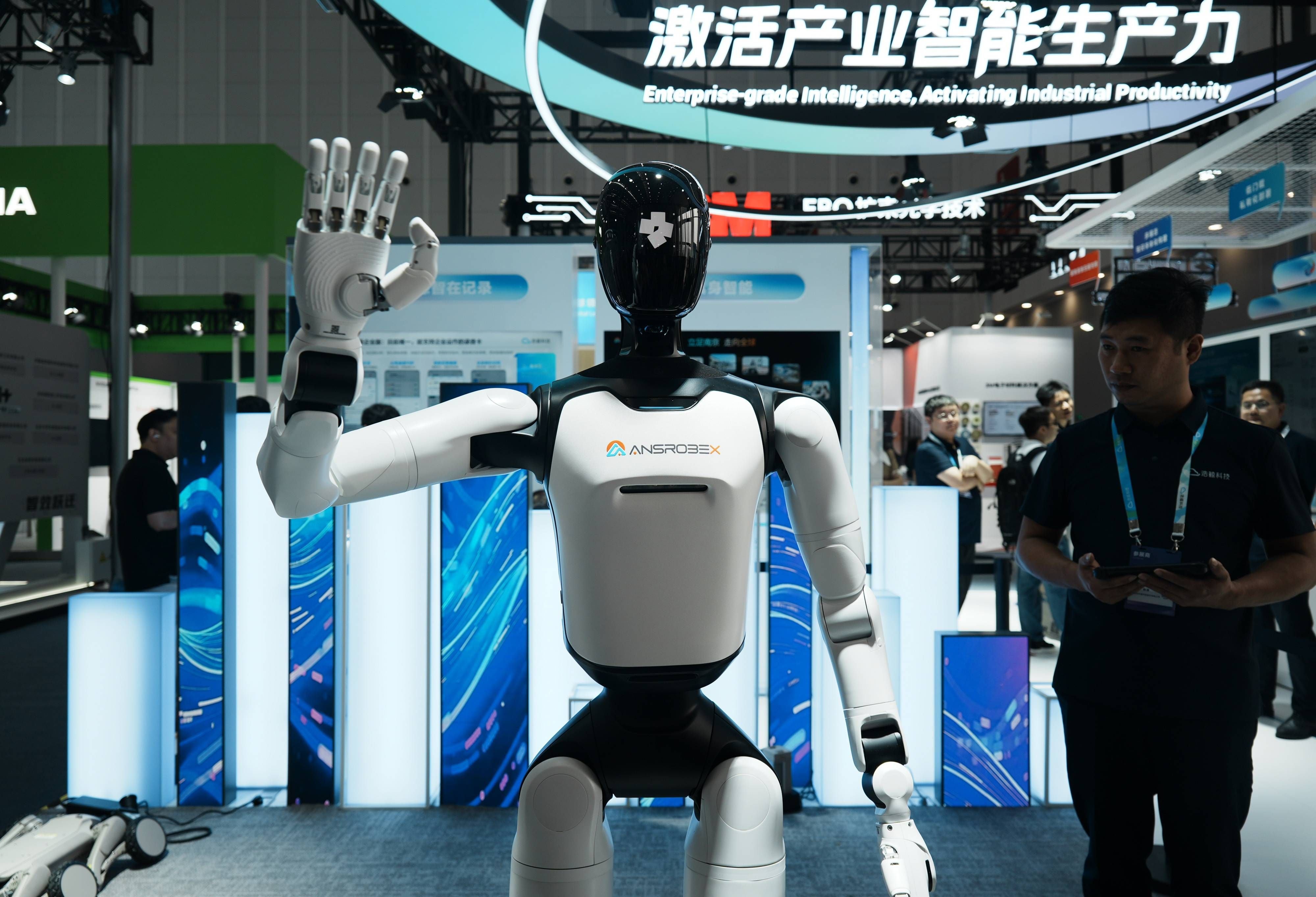 Ein humanoider Roboter grüßt Besucher auf einer Technikmesse, im Hintergrund stehen mehrere Menschen.