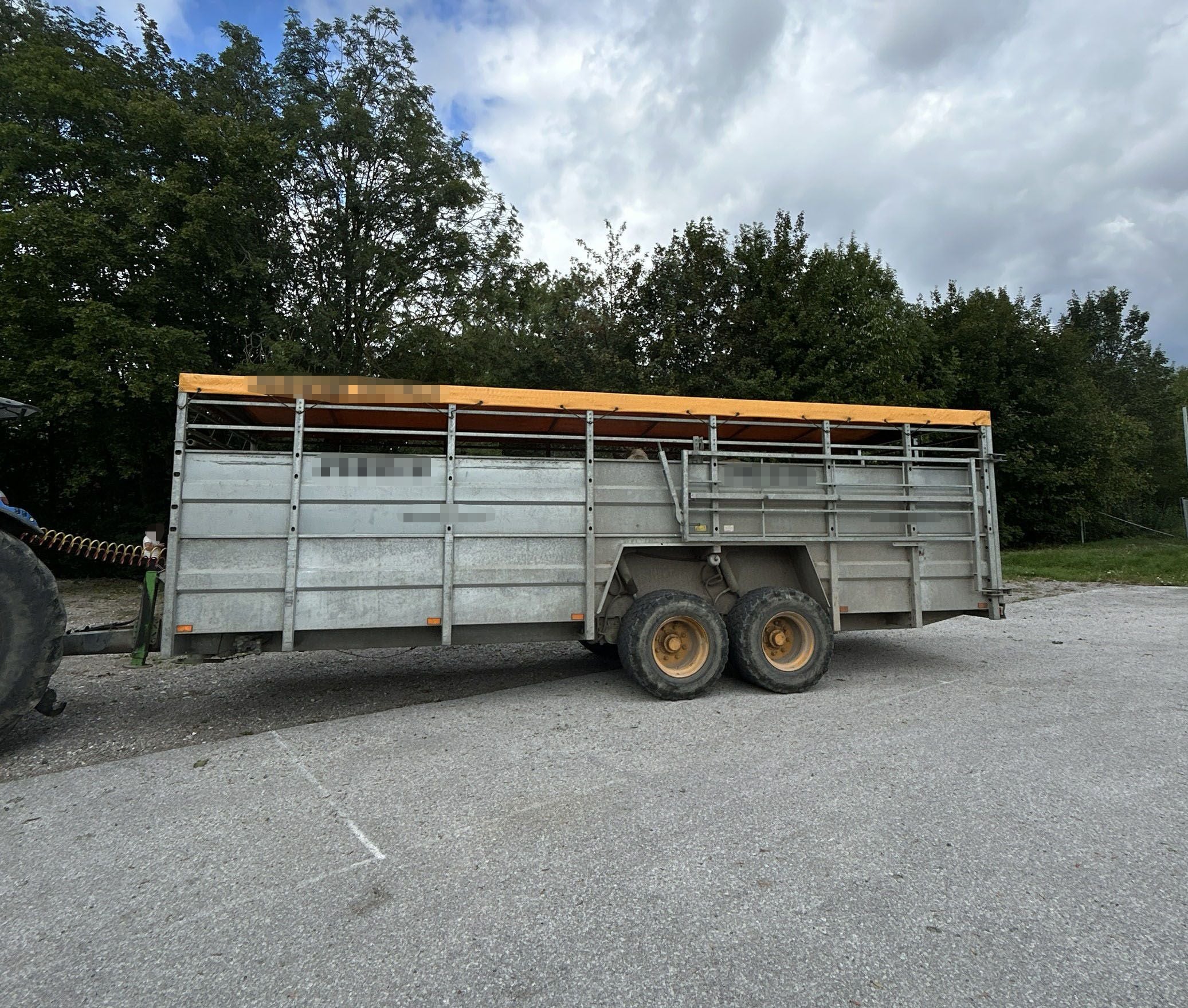 Großer Viehanhänger mit gelbem Dach steht auf einem Parkplatz vor Bäumen und bewölktem Himmel.
