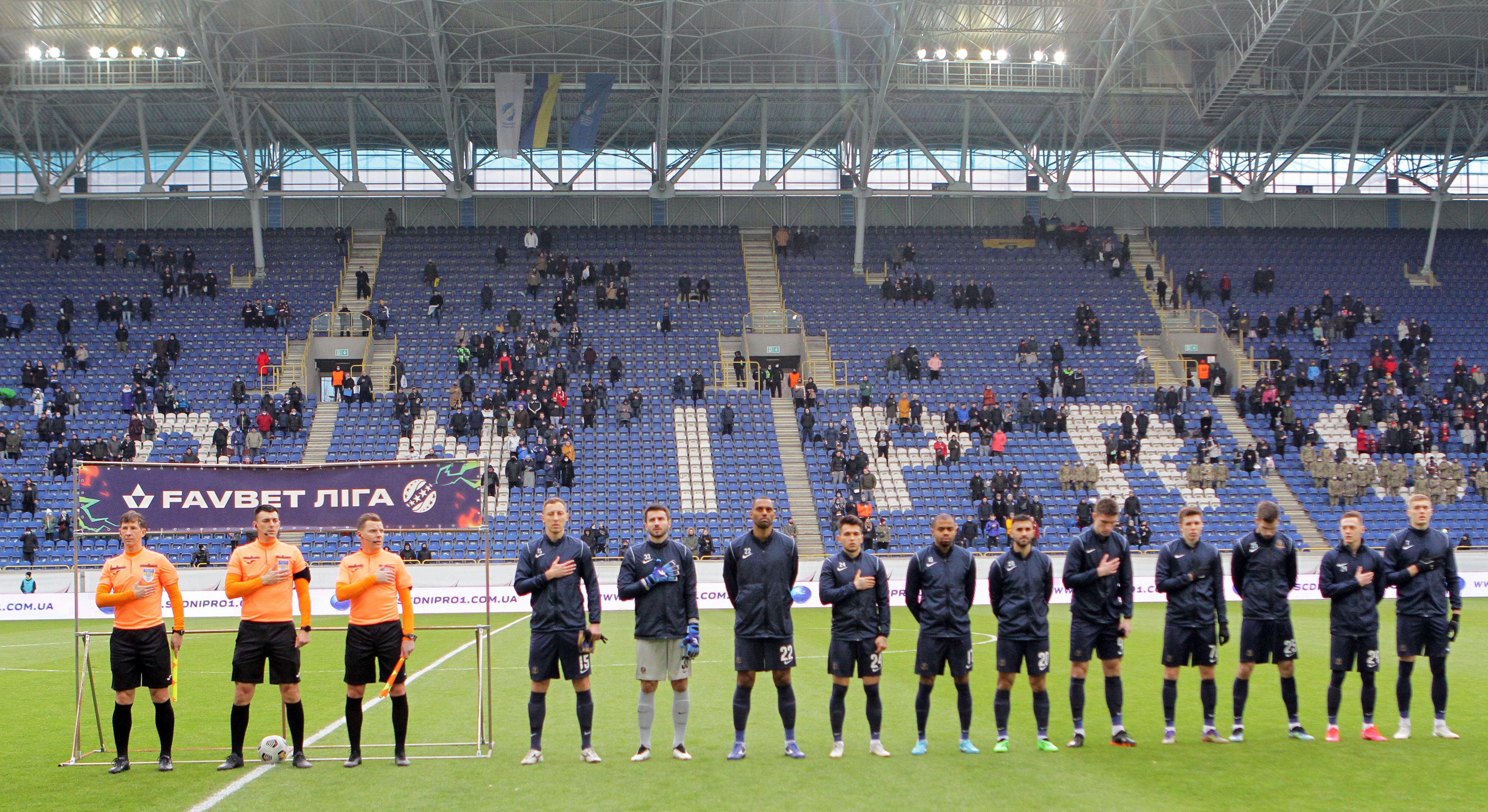 Schiedsrichter und Spieler stehen vor dem Anpfiff im Stadion in einer Reihe auf dem Rasen.